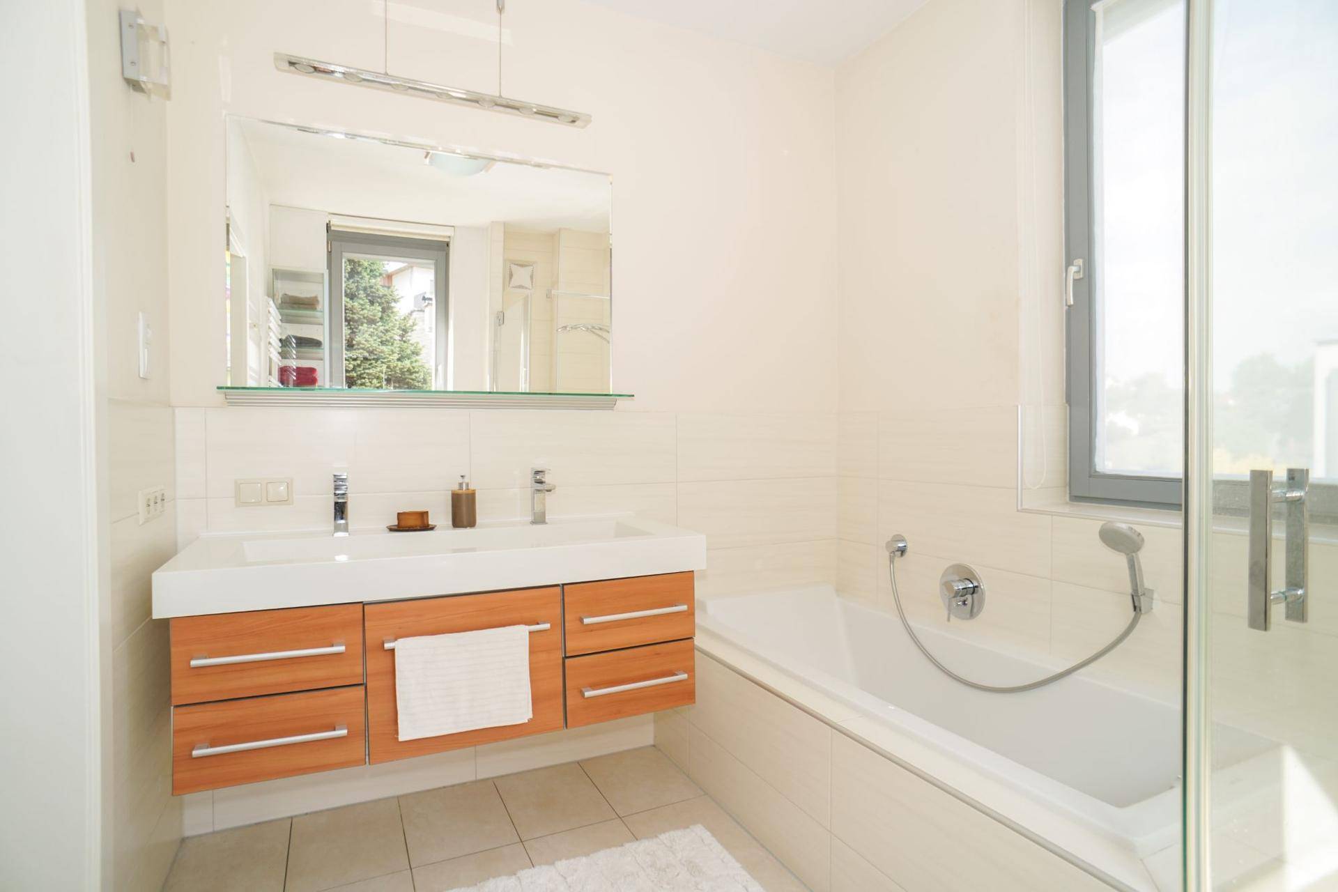 Modernes Badezimmer mit Doppelwaschbecken, Badewanne und Fenster für Tageslicht.