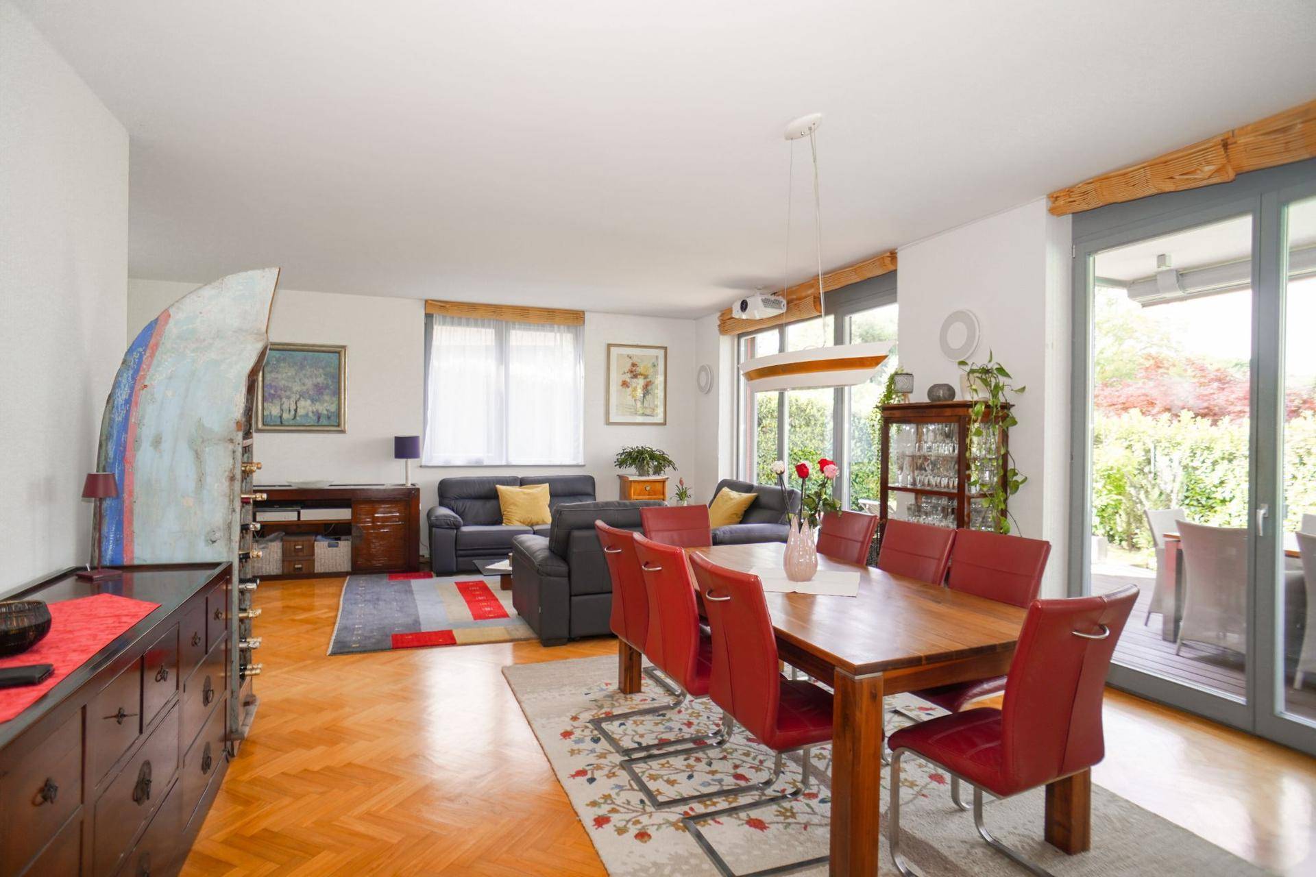 Heller Wohn- und Essbereich mit Parkettboden, rotem Esstisch und Zugang zur Terrasse.