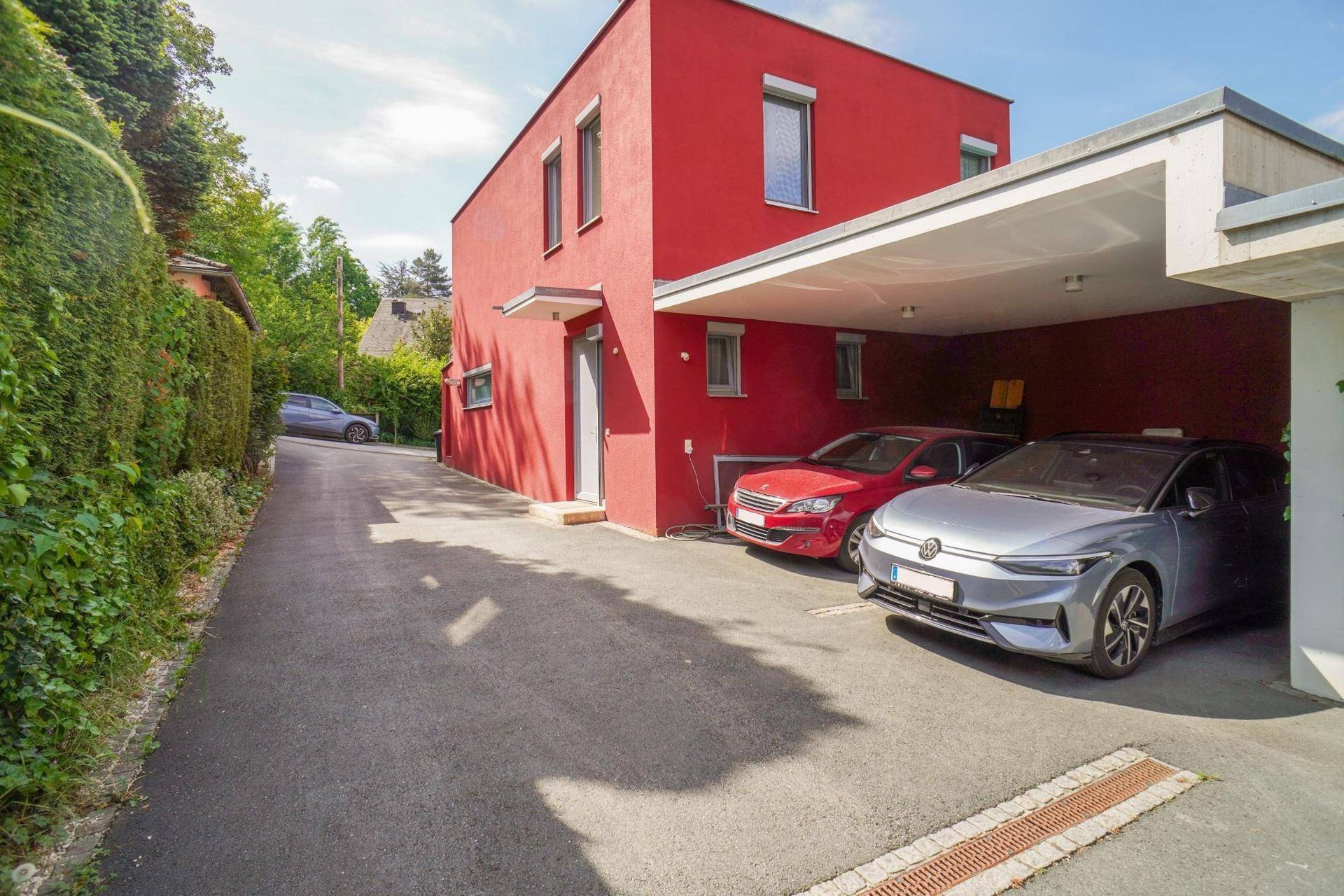 Überdachter Carport mit zwei Fahrzeugen und Zufahrt zum modernen Haus.