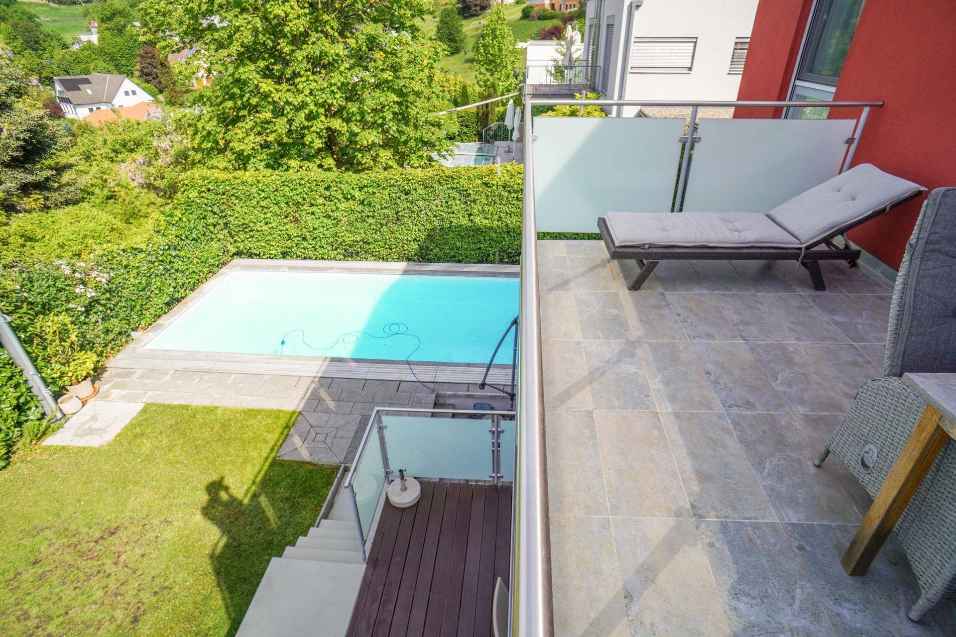 Balkon mit Liegestuhl und Blick auf den Pool und den Gartenbereich des Hauses.