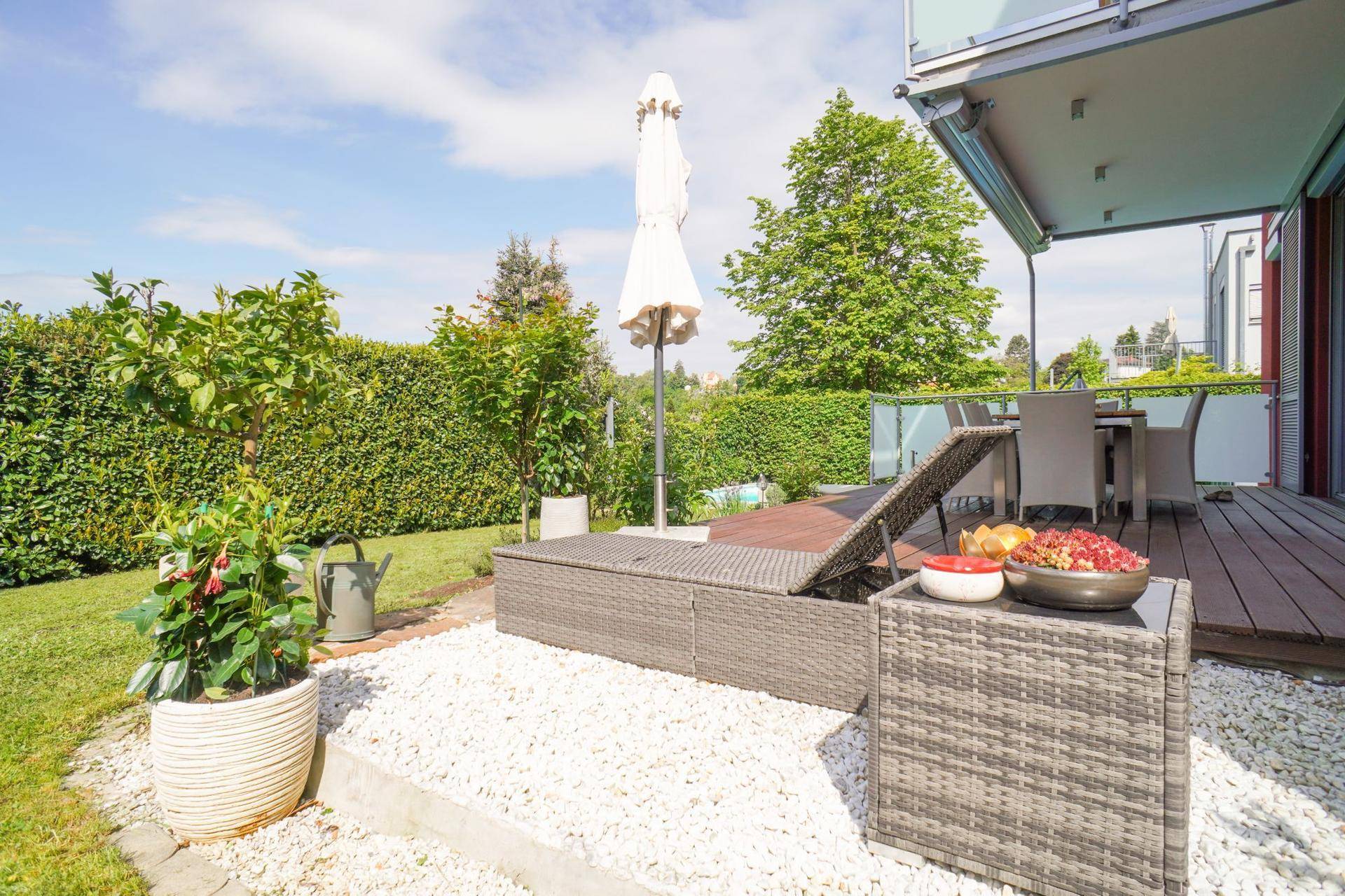 Sonniger Terrassenbereich mit Liegestuhl, Sonnenschirm und Blick auf den grünen Garten.