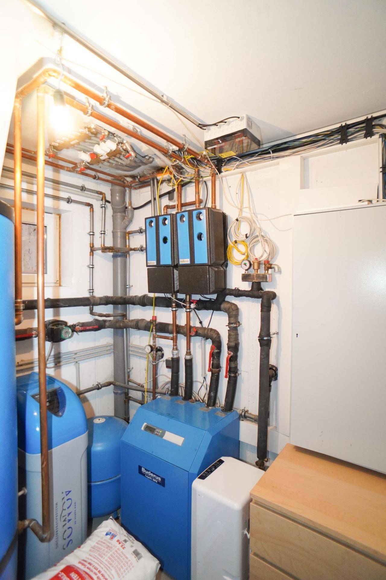 Technikraum im Untergeschoss mit Heizungsanlage, Rohren und elektrischen Installationen.