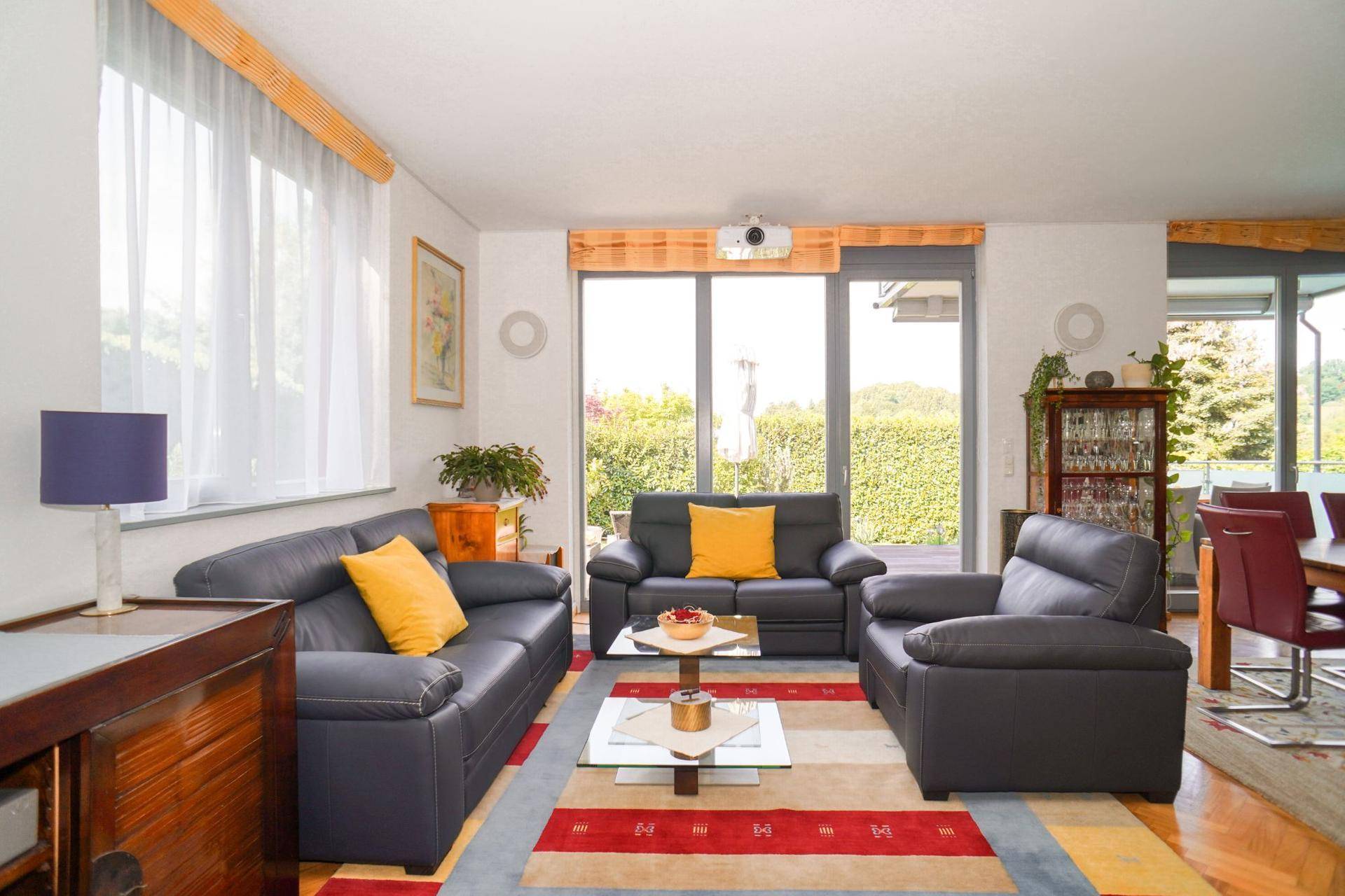 Gemütliches Wohnzimmer mit dunklen Ledersofas, farbigem Teppich und Blick ins Grüne.