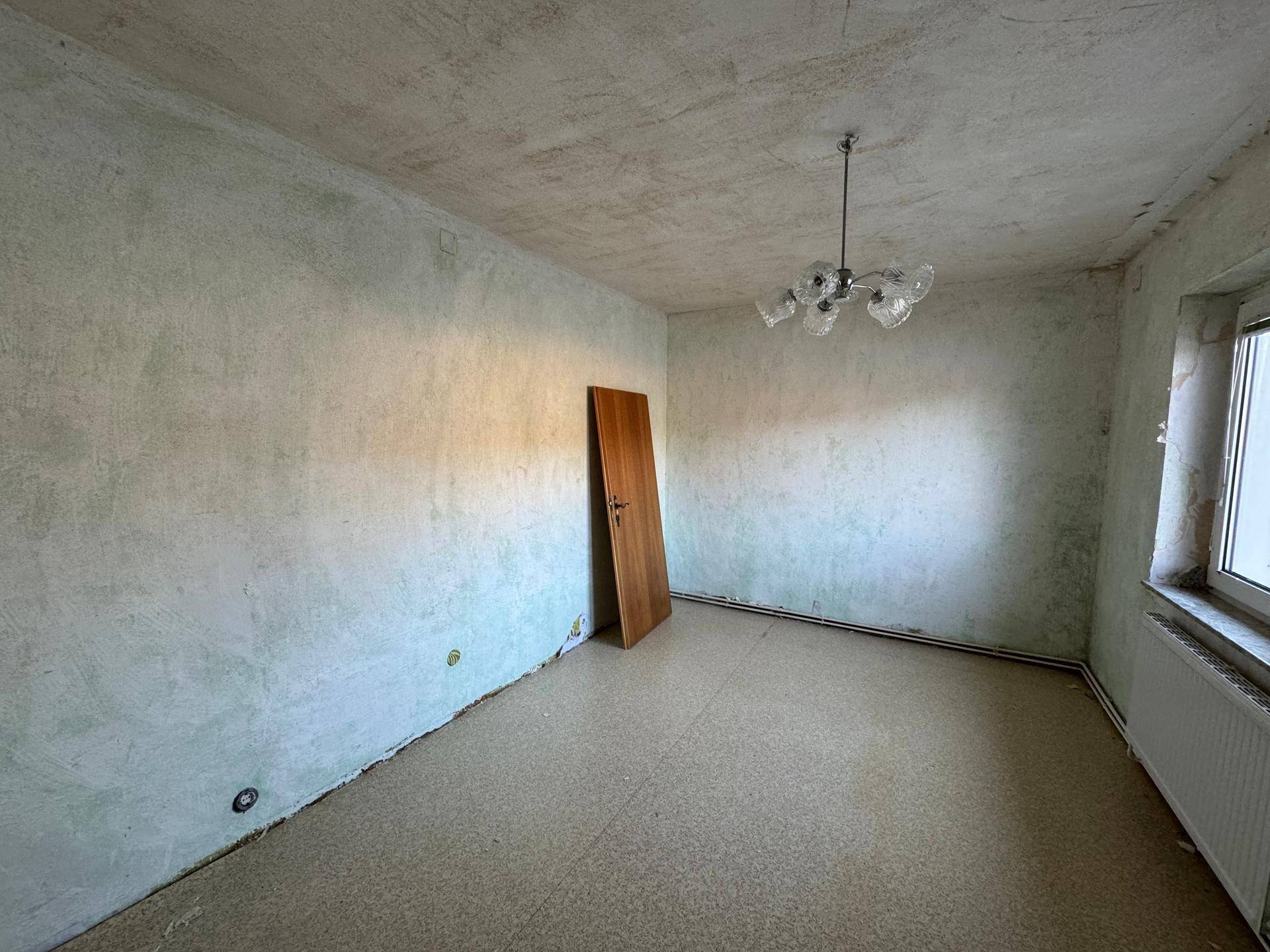 Leerer Raum mit alter Tapete, einem Fenster und einer Deckenleuchte, wartet auf Renovierung.