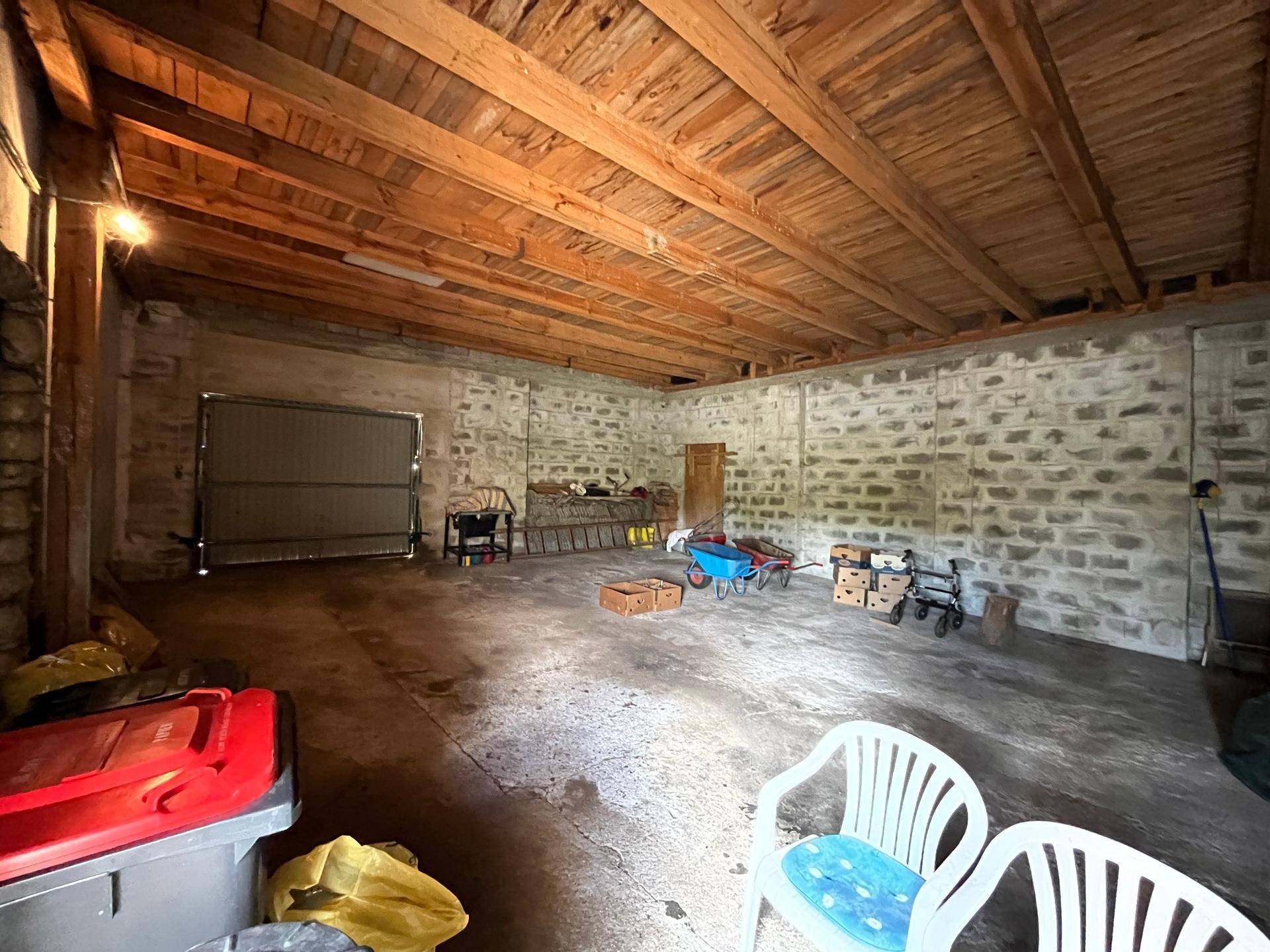 Geräumiger Garagen- oder Abstellraum mit unverputzten Steinwänden und sichtbarer Holzdecke.