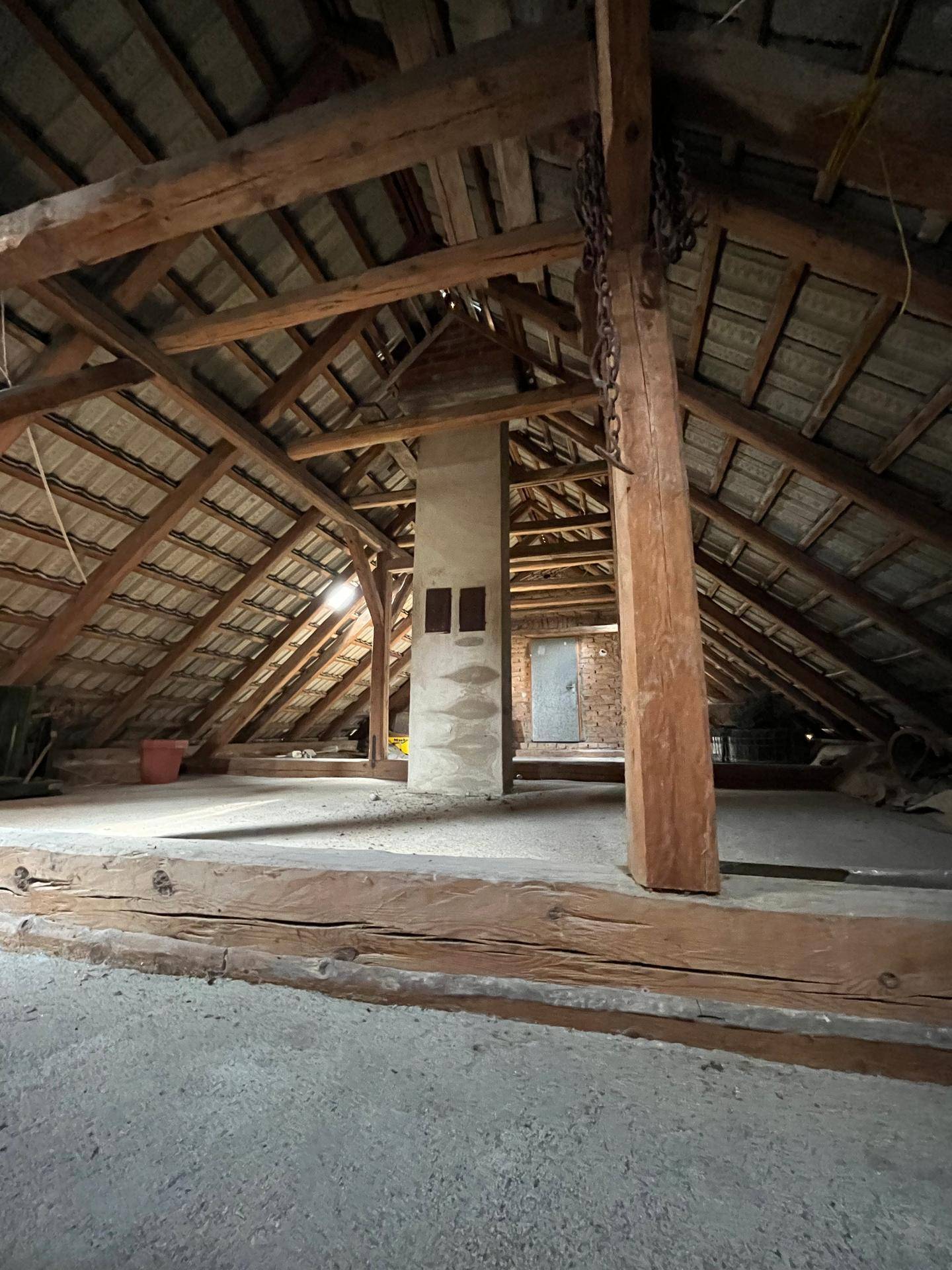 Großer Dachboden mit sichtbarer Holzbalkenkonstruktion und unfertigem Zustand, ideal für Ausbau.