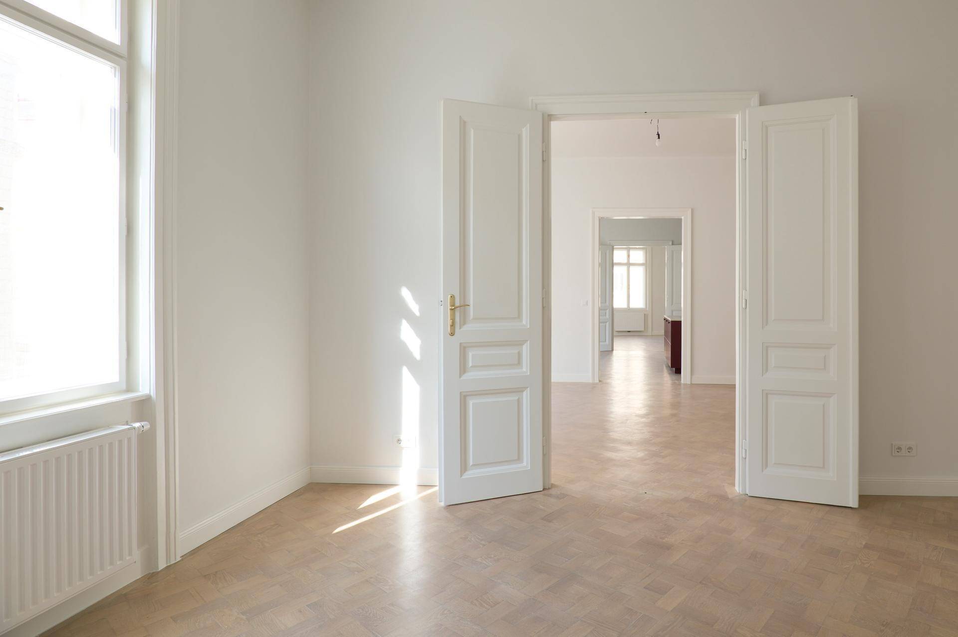 Lichtdurchfluteter Raum mit Fischgrätparkett und hohen Flügeltüren, der den Blick in weitere Zimmer freigibt.