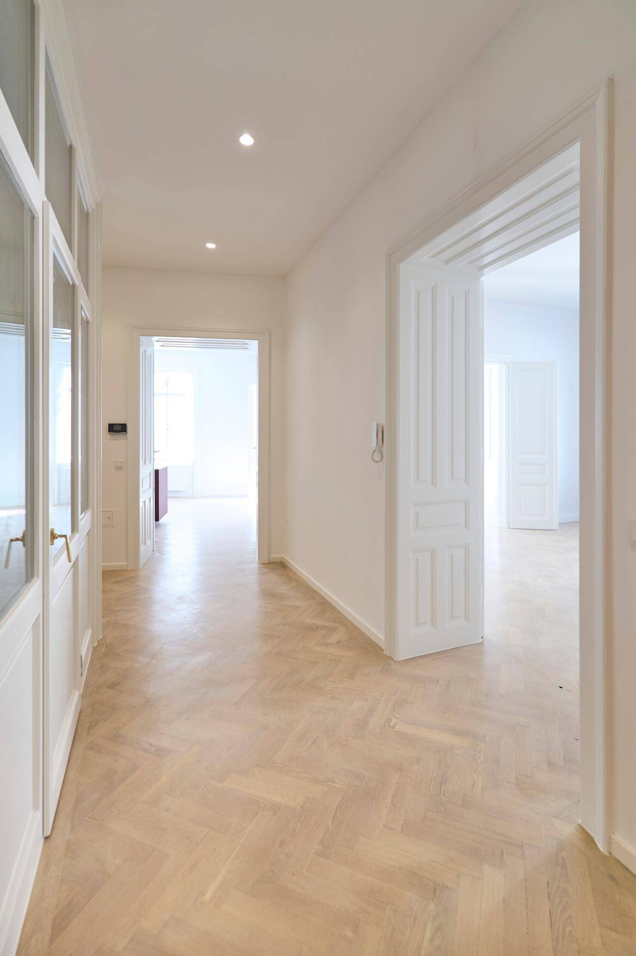 Geräumiger Flur mit hellem Fischgrätparkett und hohen Türen, der zu verschiedenen Zimmern der Wohnung führt.