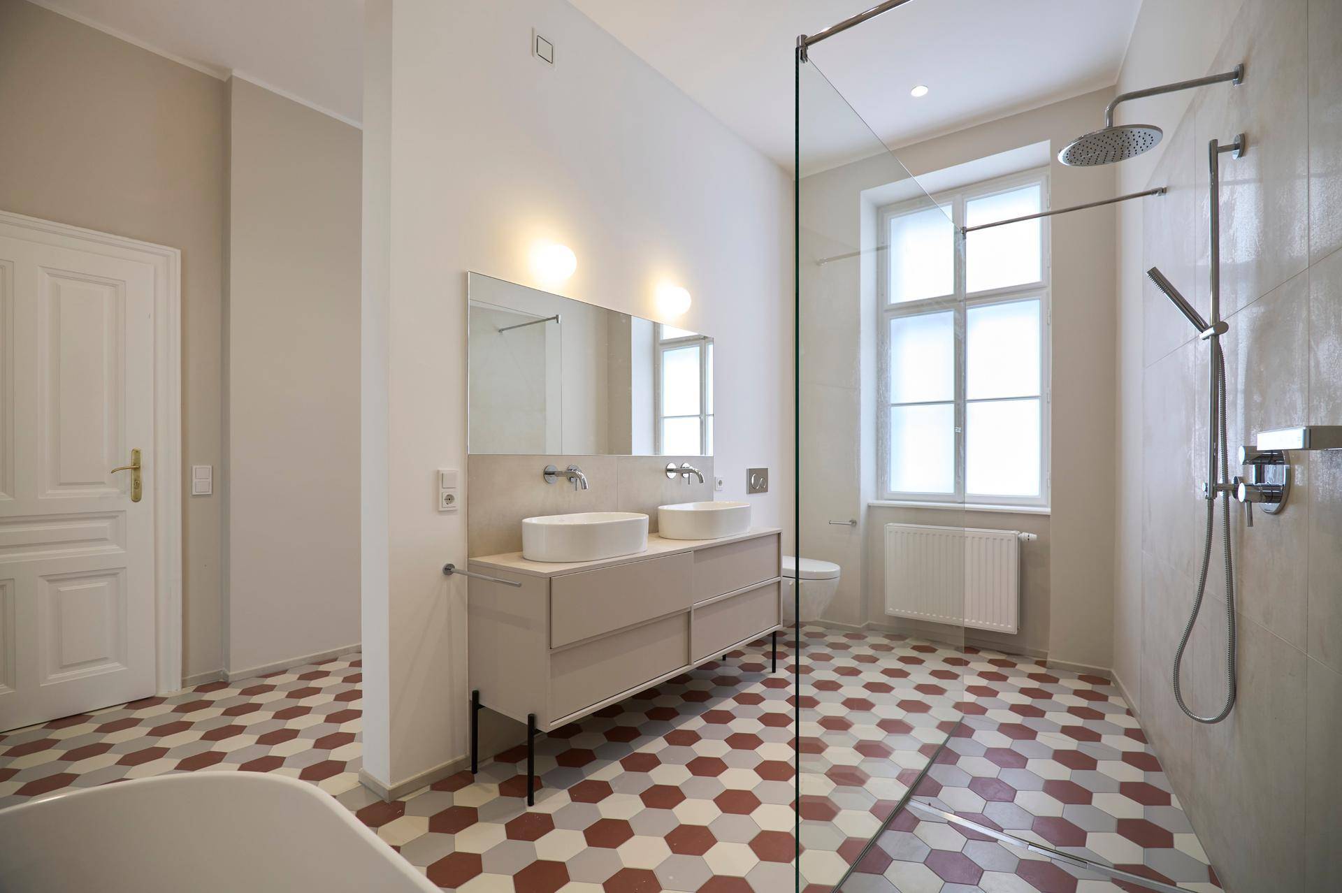 Helles Badezimmer mit Doppelwaschbecken, begehbarer Dusche, Fenster und einem auffälligen sechseckigen Fliesenboden.
