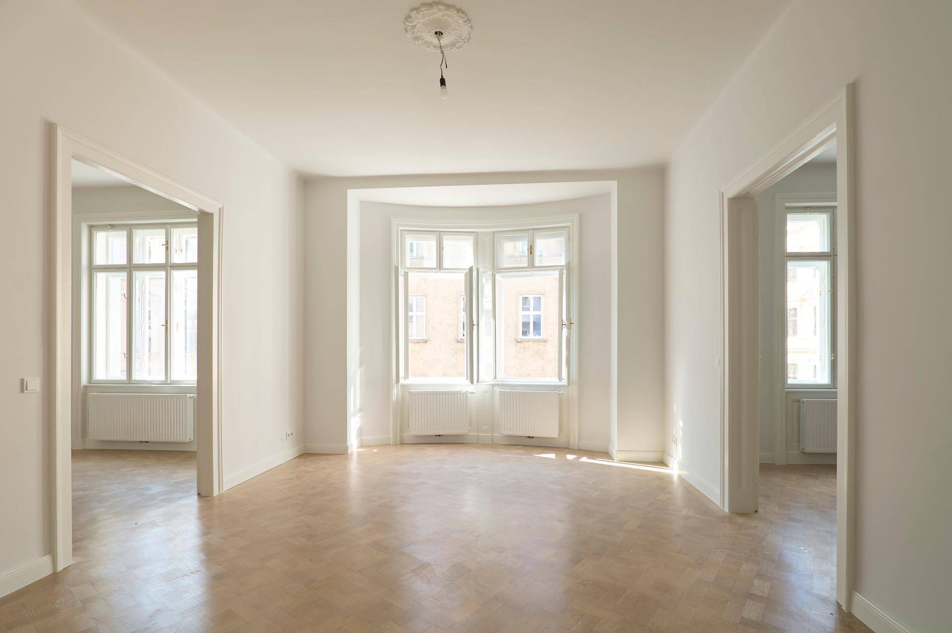 Helles, leeres Zimmer mit Fischgrätparkett, hohen Fenstern und Stuckdecke, bereit zur individuellen Gestaltung.