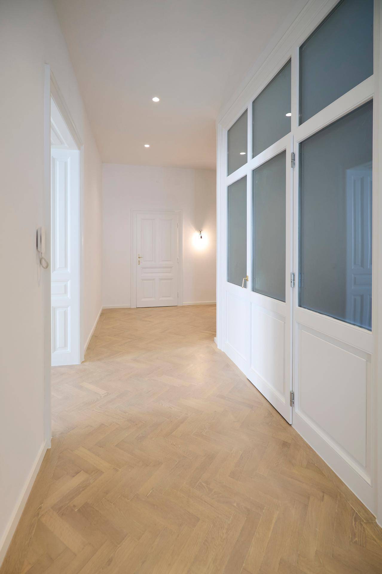 Heller Flur mit Fischgrätparkett und einer Wand aus Glasbausteinen, die Licht in angrenzende Räume lässt.