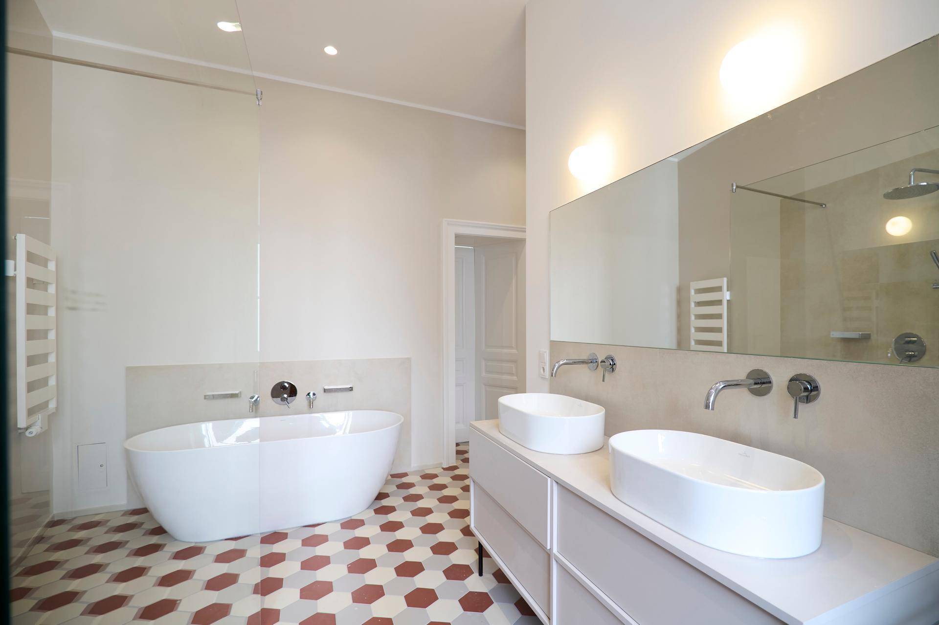 Elegantes Badezimmer mit Doppelwaschbecken, großem Spiegel und freistehender Badewanne auf einem gemusterten Fliesenboden.