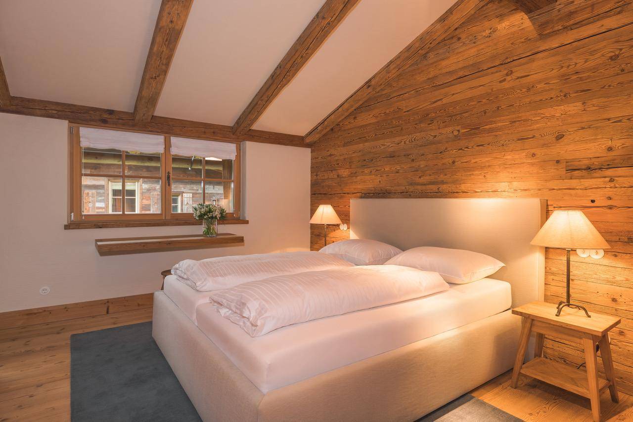 Schlafzimmer im alpinen Stil mit Holzwänden, Deckenbalken und einem Fenster mit Blick nach draußen.