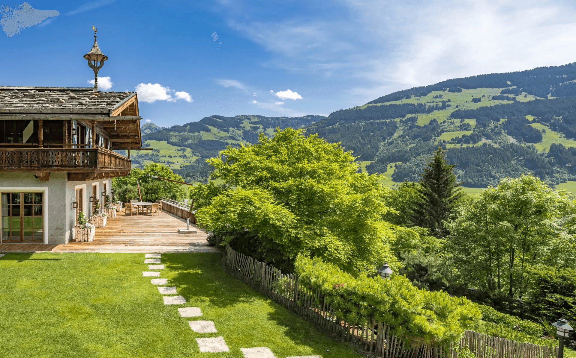 Seitlicher Blick auf das Chalet mit großer Holzterrasse, gepflegtem Rasen und Bergblick.