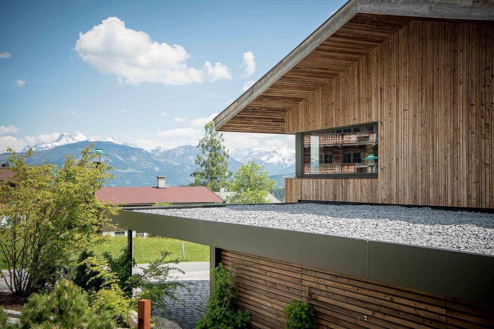 Flachdachbereich mit Kies und einem Fenster, das einen weiten Blick auf die schneebedeckten Berge bietet.