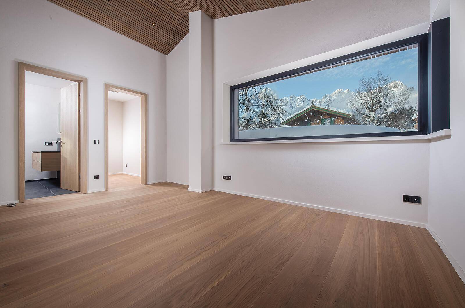 Geräumiges Schlafzimmer mit Holzboden und einem breiten Fenster, das einen malerischen Bergblick bietet.