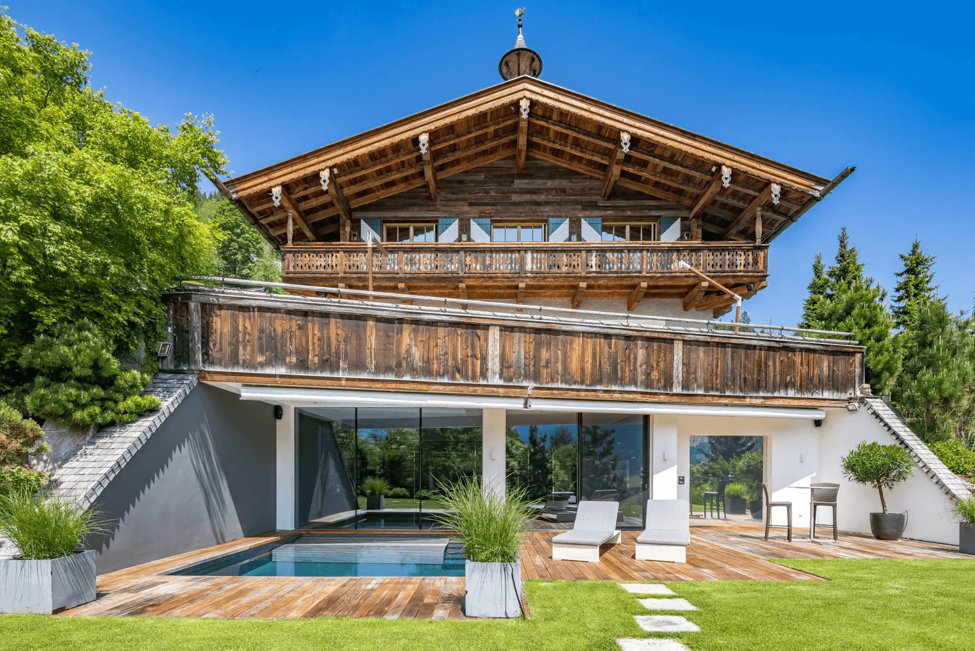 Frontansicht des Chalets mit großzügigem Außenpool, Holzdeck und gepflegtem Rasenbereich.