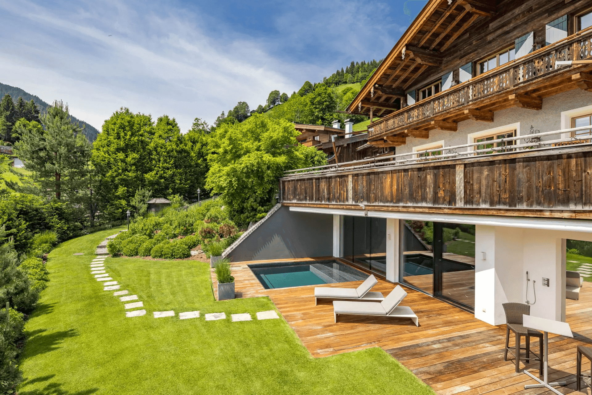 Chalet mit Außenpool, Holzterrasse, grünem Rasen und Steinpfad in idyllischer Berglandschaft.