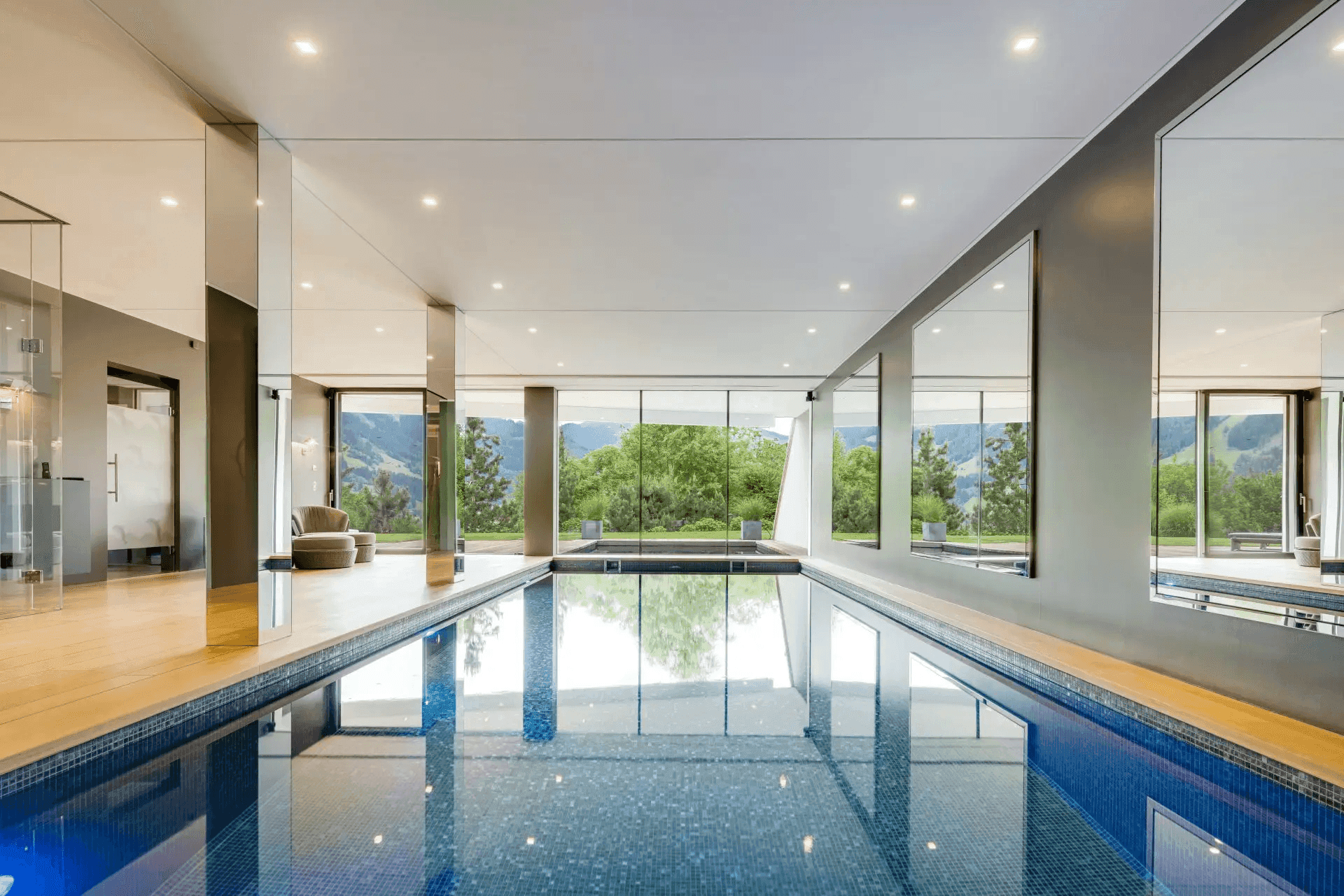 Moderner Innenpool mit großen Fenstern und Panoramablick auf die grüne Landschaft.