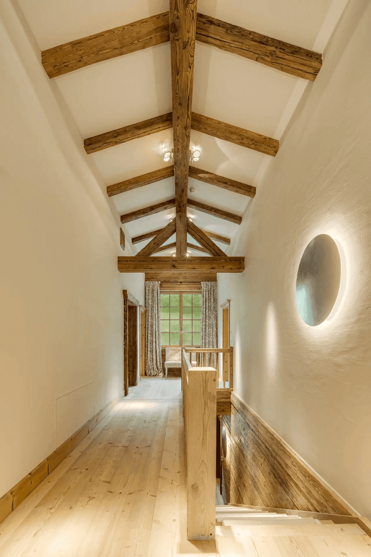 Heller Flur mit Holzbalkendecke, Holzboden und modernem Wandlicht.