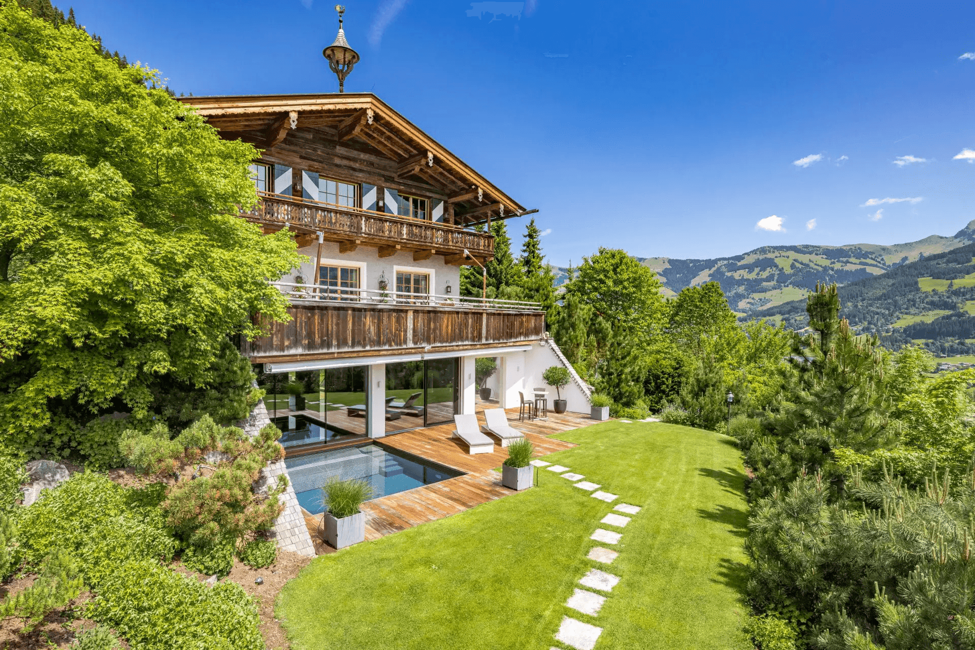 Elegantes Chalet mit modernem Außenpool, weitläufigem Rasen und malerischem Bergblick unter blauem Himmel.