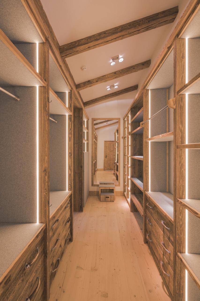 Geräumiger begehbarer Kleiderschrank mit maßgefertigten Holzregalen und integrierter Beleuchtung.
