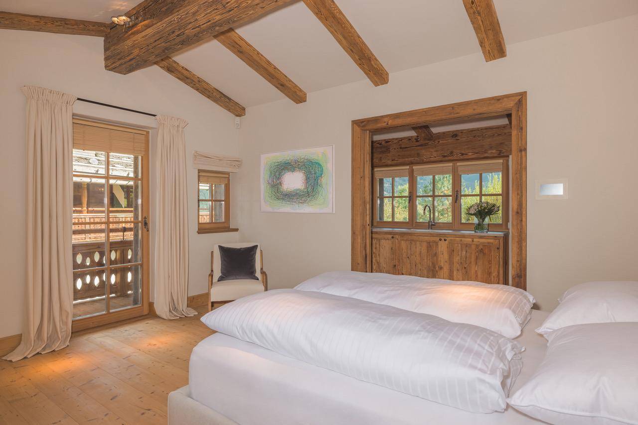 Gemütliches Schlafzimmer mit Holzbalken, großem Bett und Blick auf die umliegende Natur.