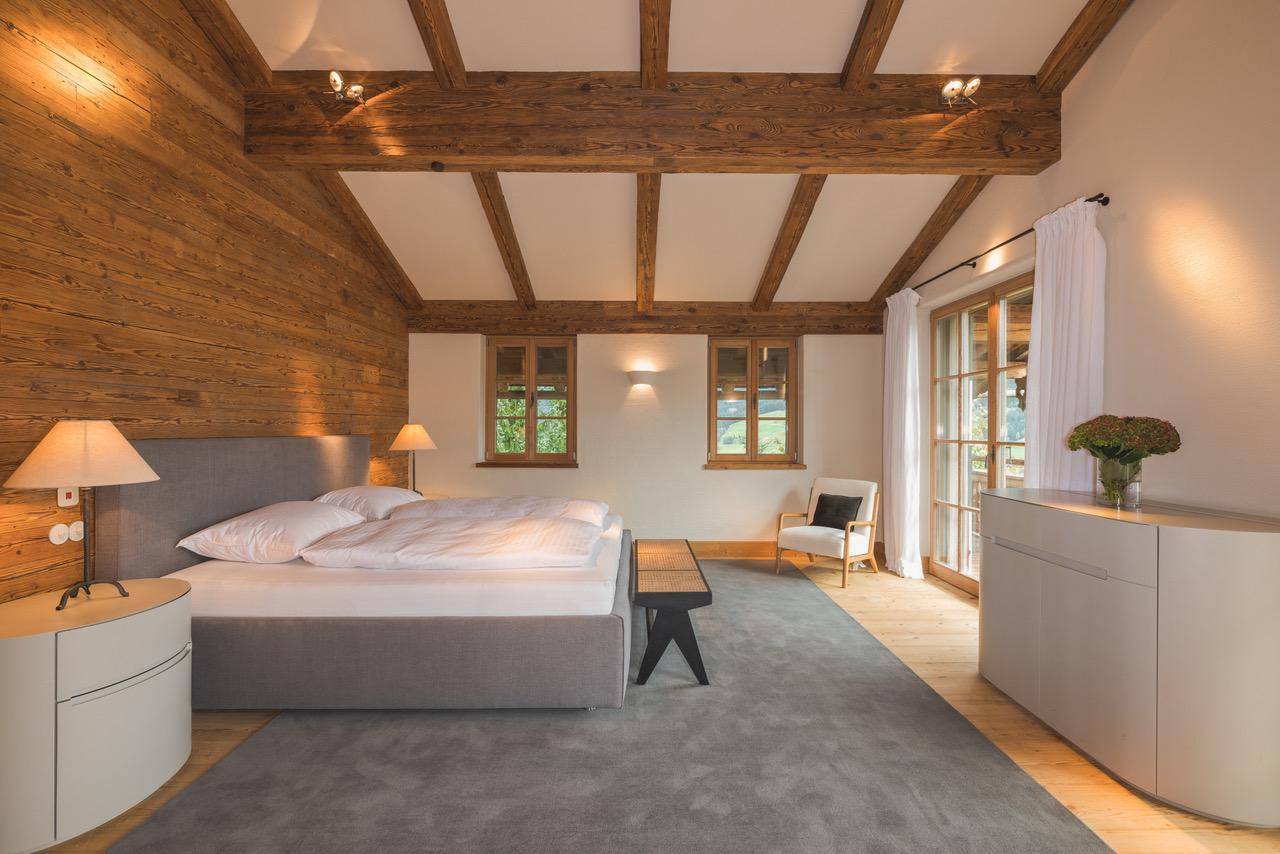 Helles Schlafzimmer mit Holzbalkendecke, großem Bett und Zugang zum Balkon.