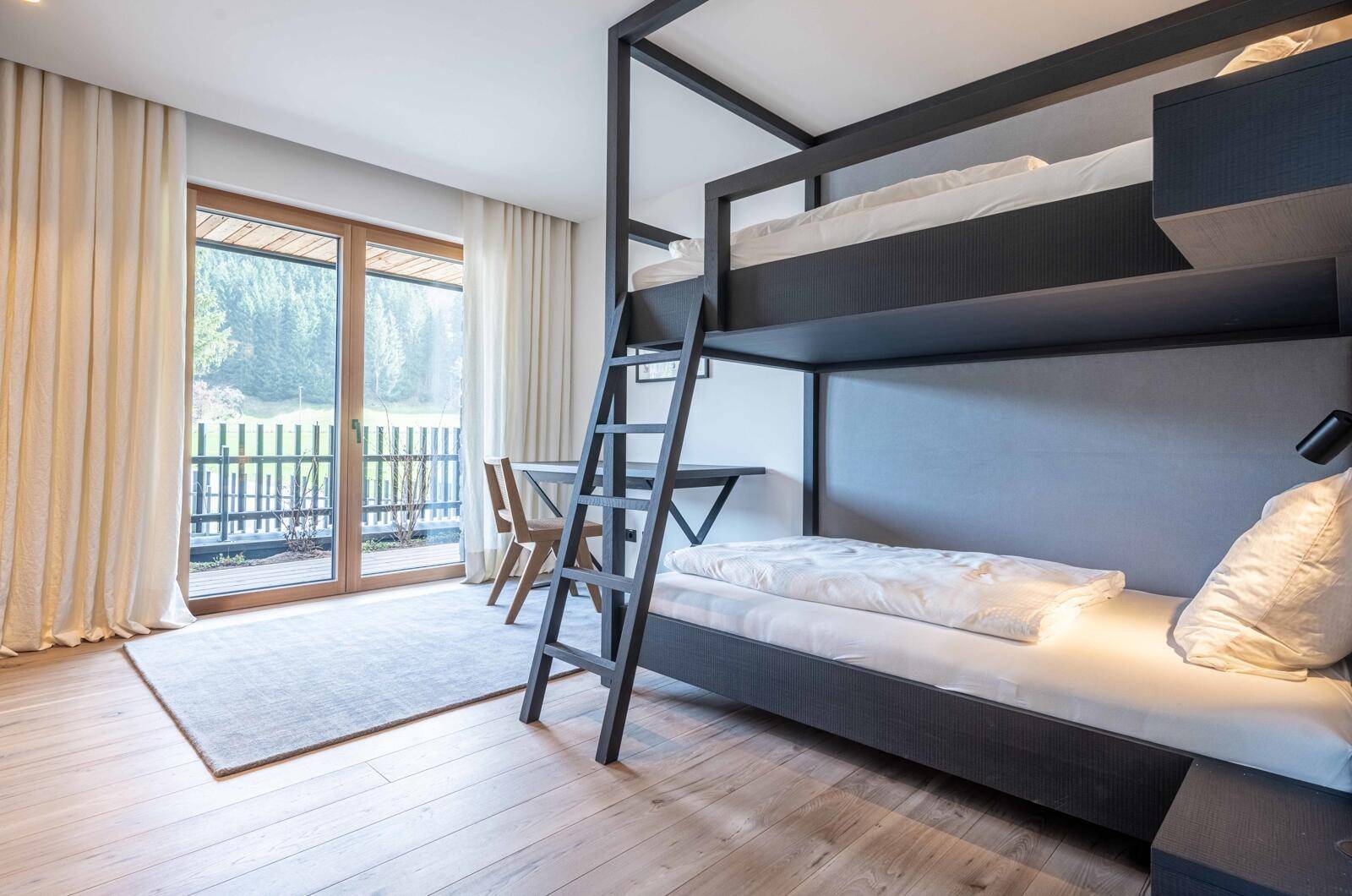 Kinderzimmer mit Etagenbett, Holzboden und Zugang zu einem Balkon mit Blick ins Grüne.
