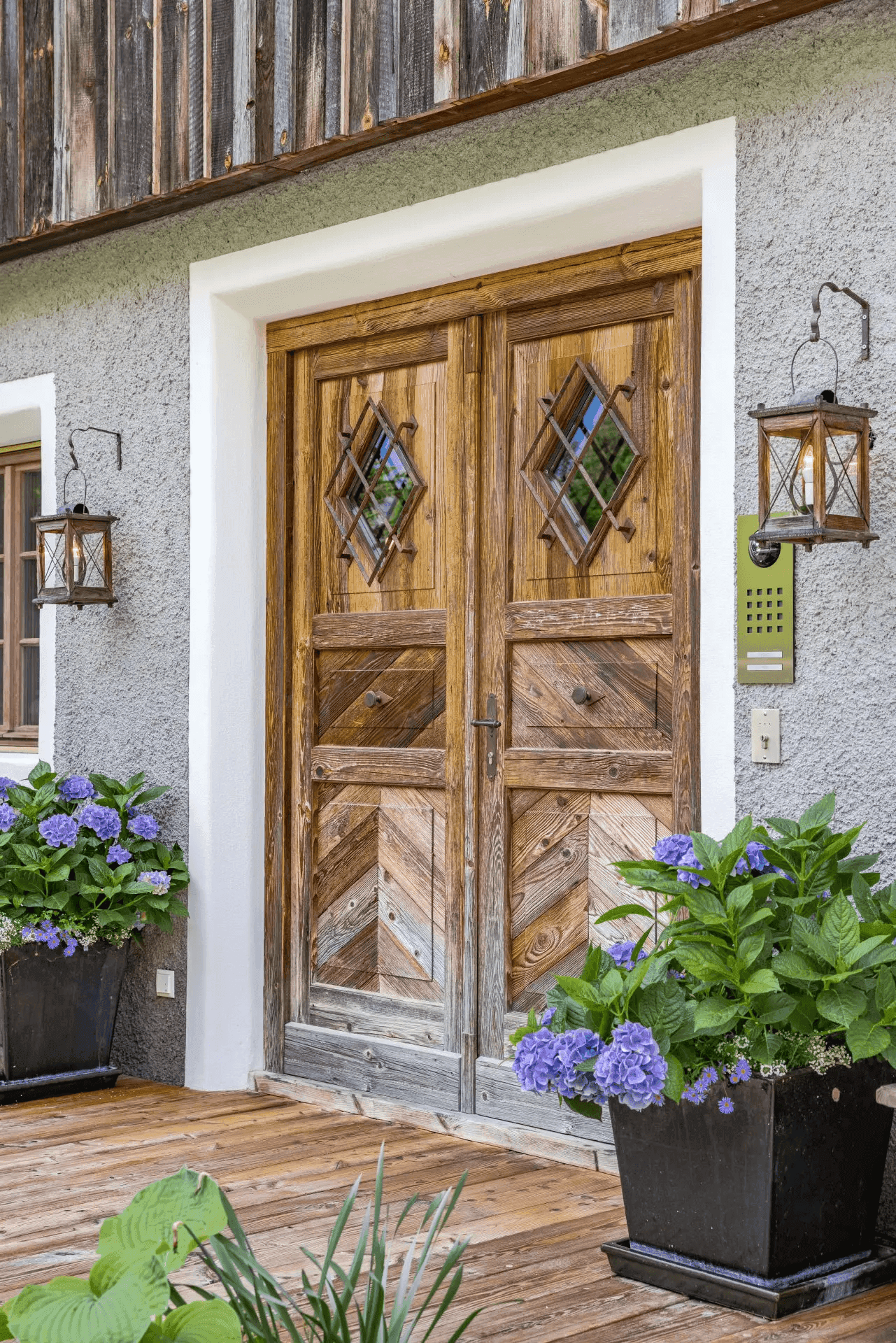 Detailaufnahme der rustikalen Holztür mit schmiedeeisernen Laternen und blühenden Hortensien.