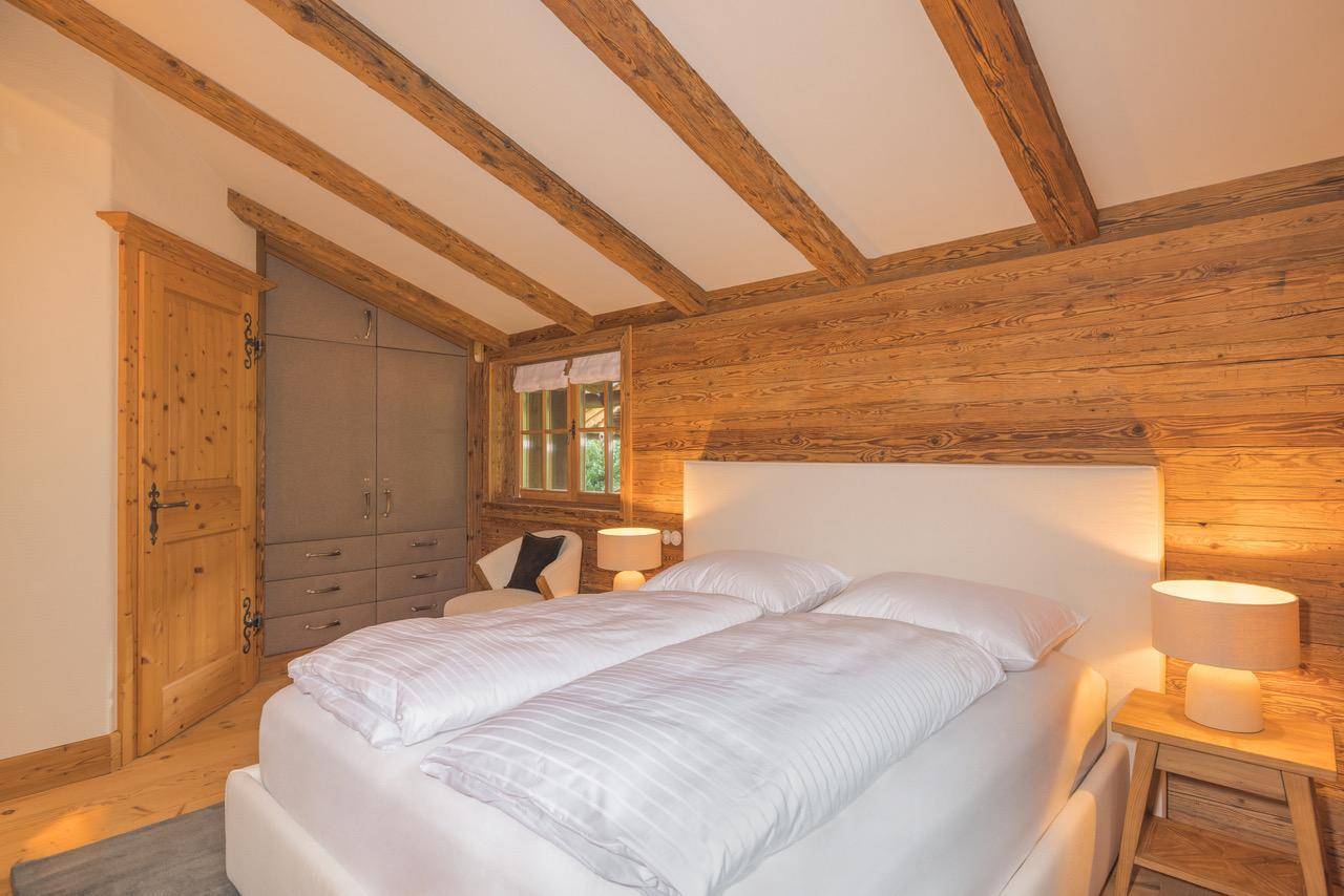 Helles Schlafzimmer mit Holzwänden, Einbauschränken und sichtbaren Deckenbalken.
