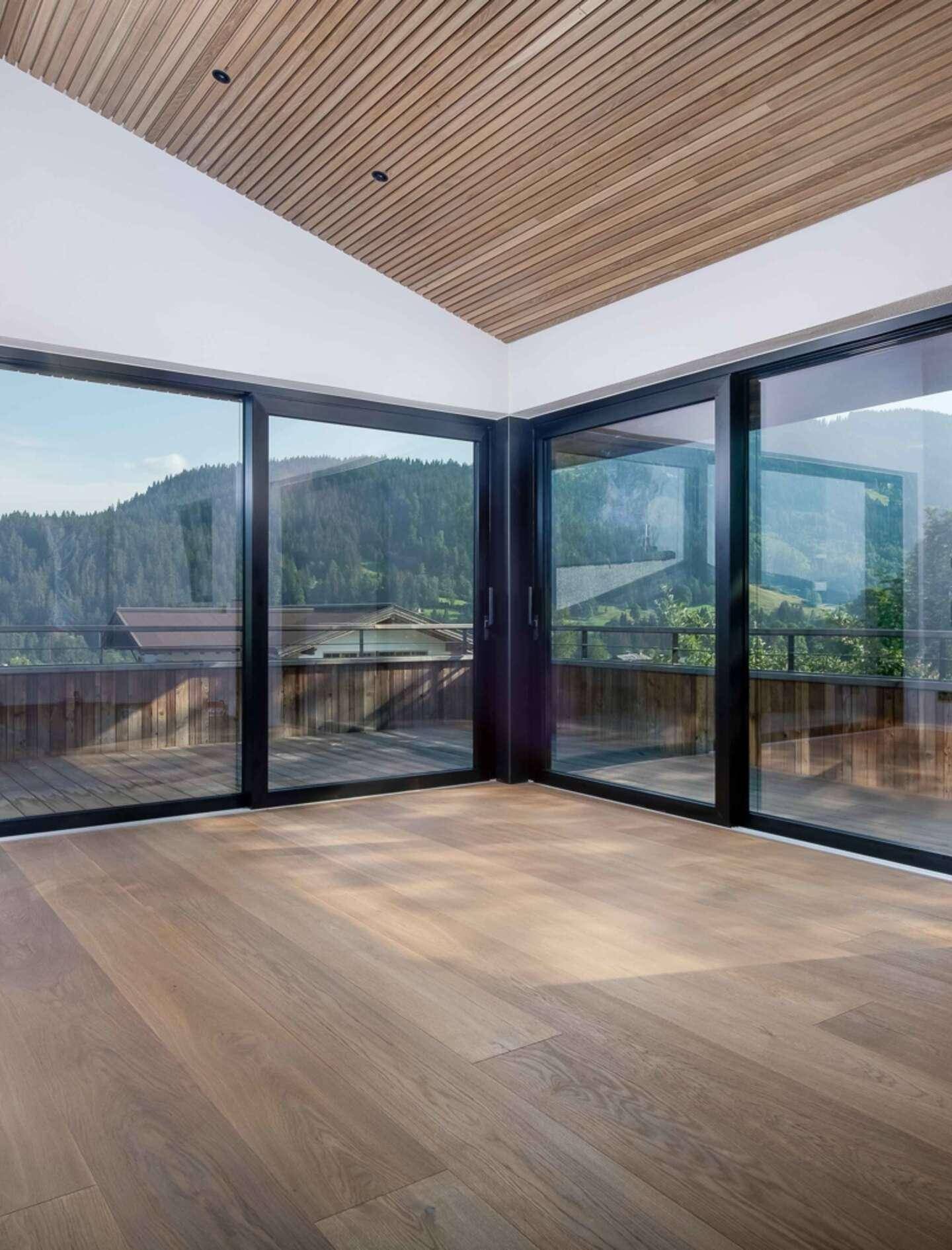 Helles Zimmer mit Holzboden und raumhohen Glastüren, die Zugang zu einem Außenbereich ermöglichen.