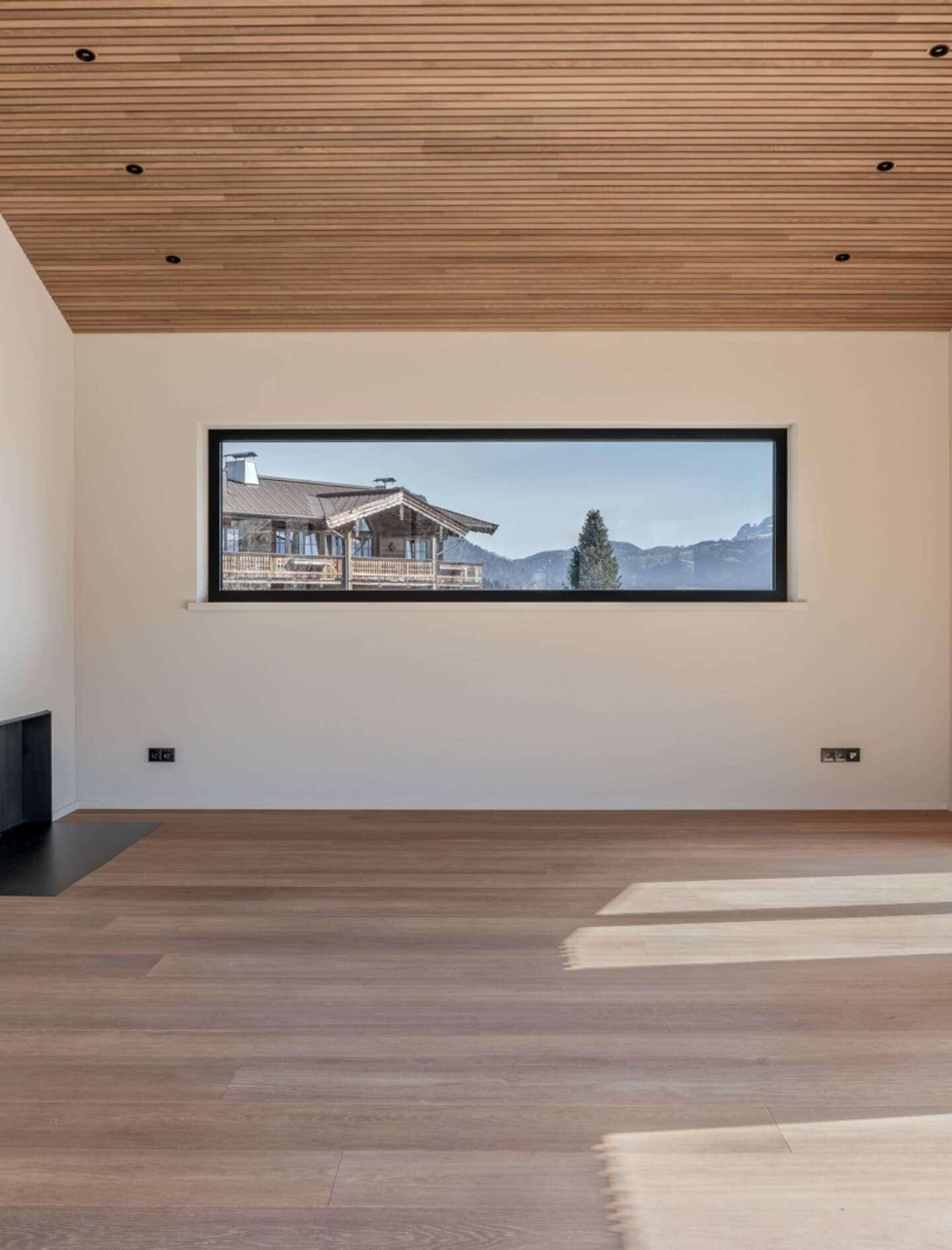 Leeres Zimmer mit Holzboden und einem langen Panoramafenster mit Blick auf die Berge.