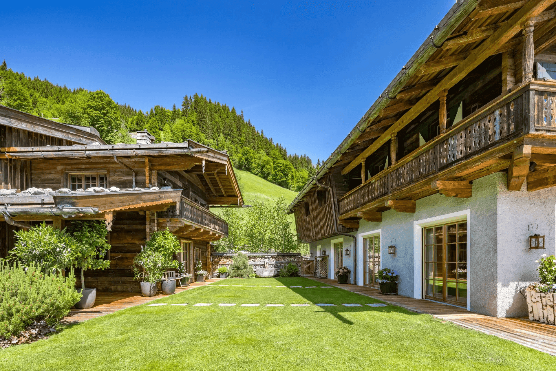 Zwei traditionelle Chalets mit gepflegtem Rasen und üppiger grüner Umgebung unter blauem Himmel.