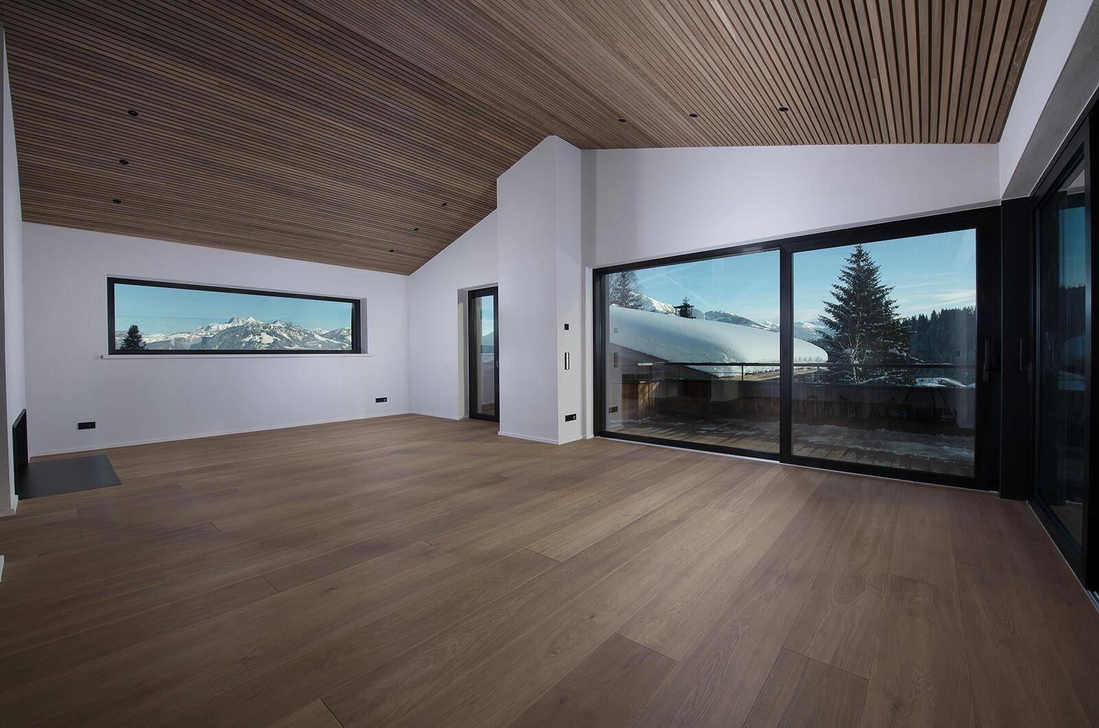 Helles, leeres Wohnzimmer mit Holzboden, hohen Decken und weitem Bergblick.