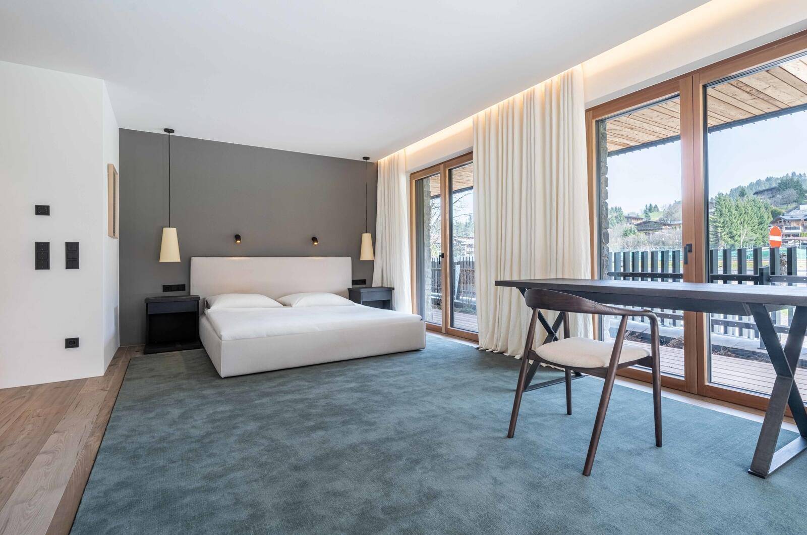 Helles Schlafzimmer mit großem Bett, Teppichboden und Zugang zu einem Balkon mit Bergblick.