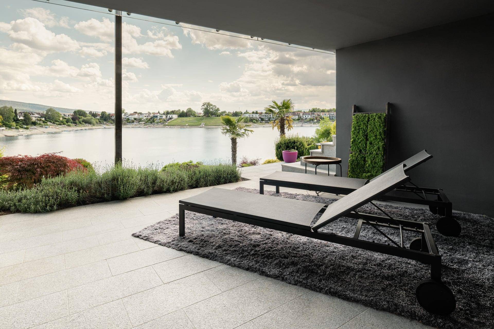 Entspannungsbereich auf der Terrasse mit Liegestühlen und Panoramablick auf den See.