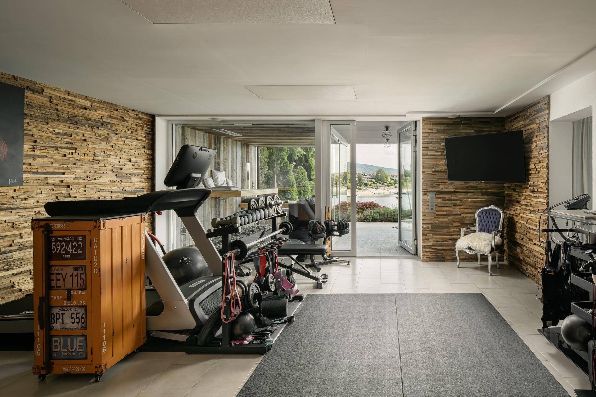Privater Fitnessraum mit Seeblick, modernen Geräten und Holzwänden für ein natürliches Ambiente.