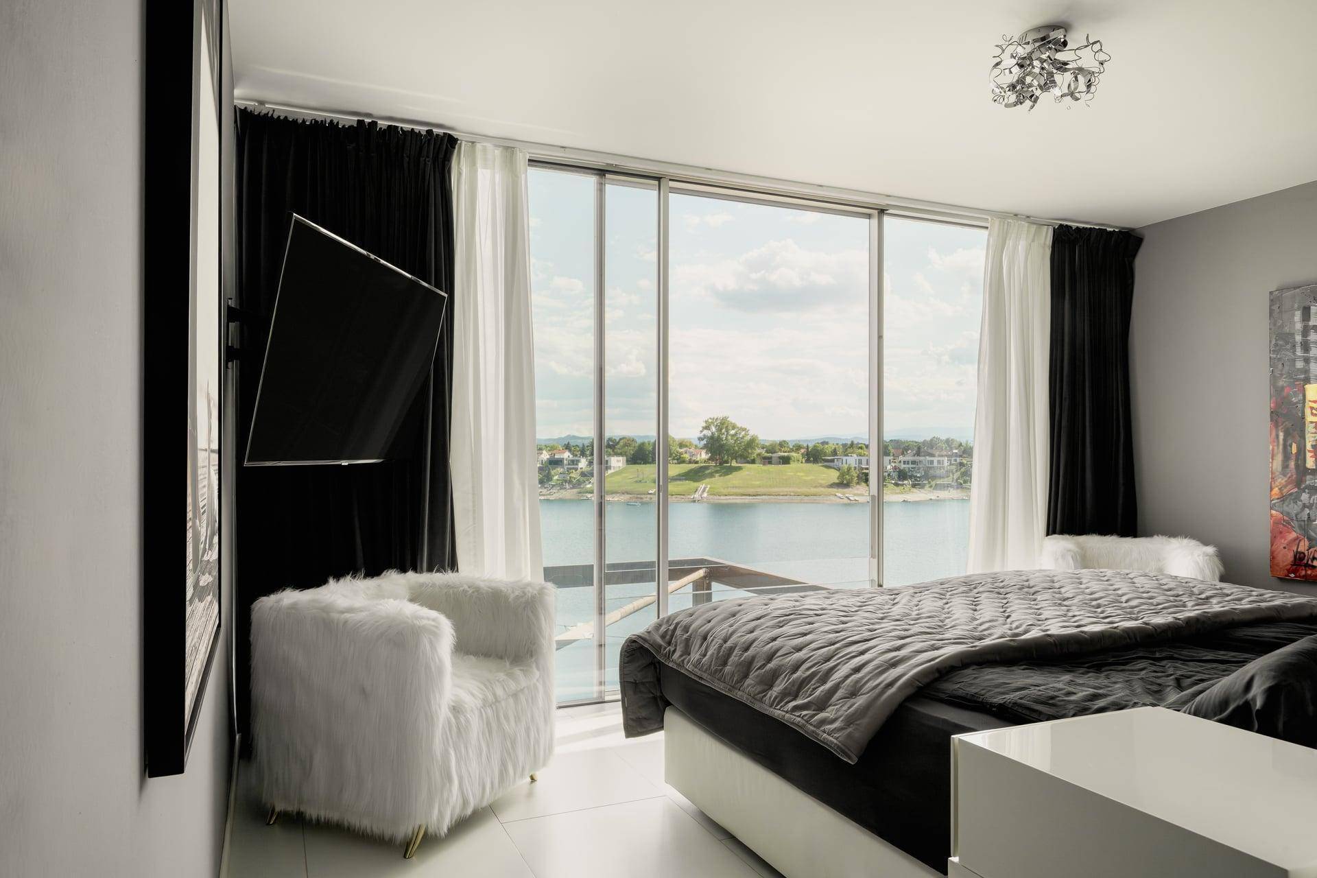 Helles Schlafzimmer mit Seeblick, großen Fenstern und luxuriöser Einrichtung.