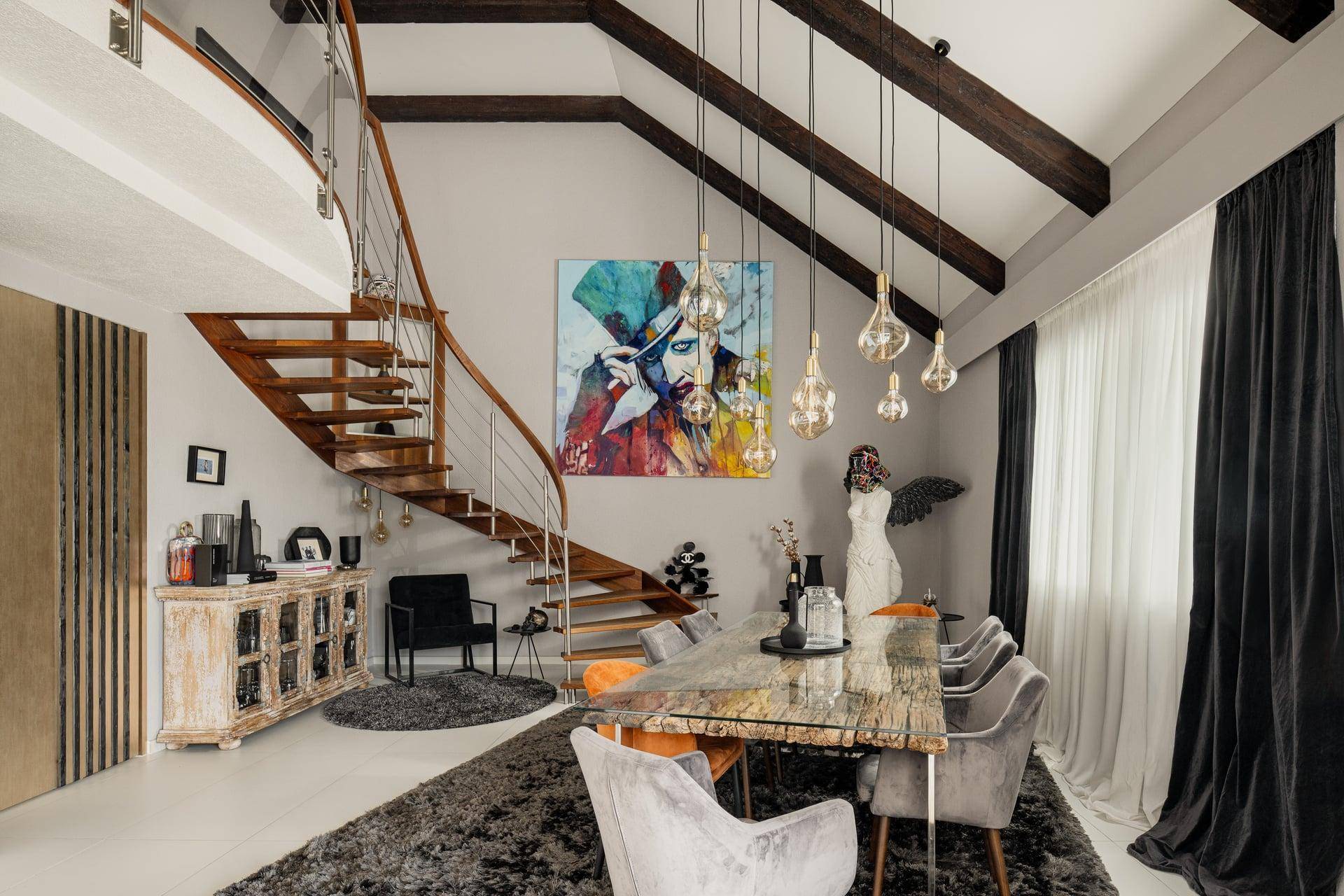 Elegantes Esszimmer mit hoher Decke, freiliegenden Holzbalken und einer geschwungenen Treppe.
