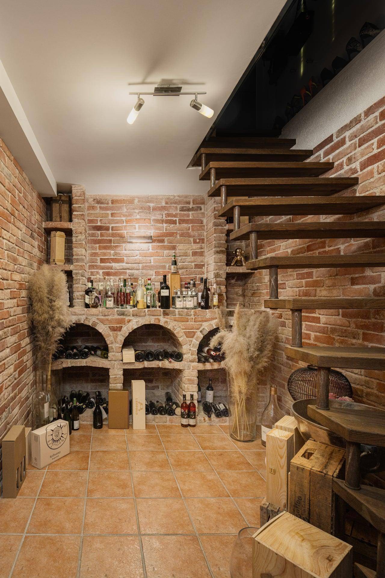 Rustikaler Weinkeller mit Ziegelwänden, Holzregalen und einer offenen Holztreppe.