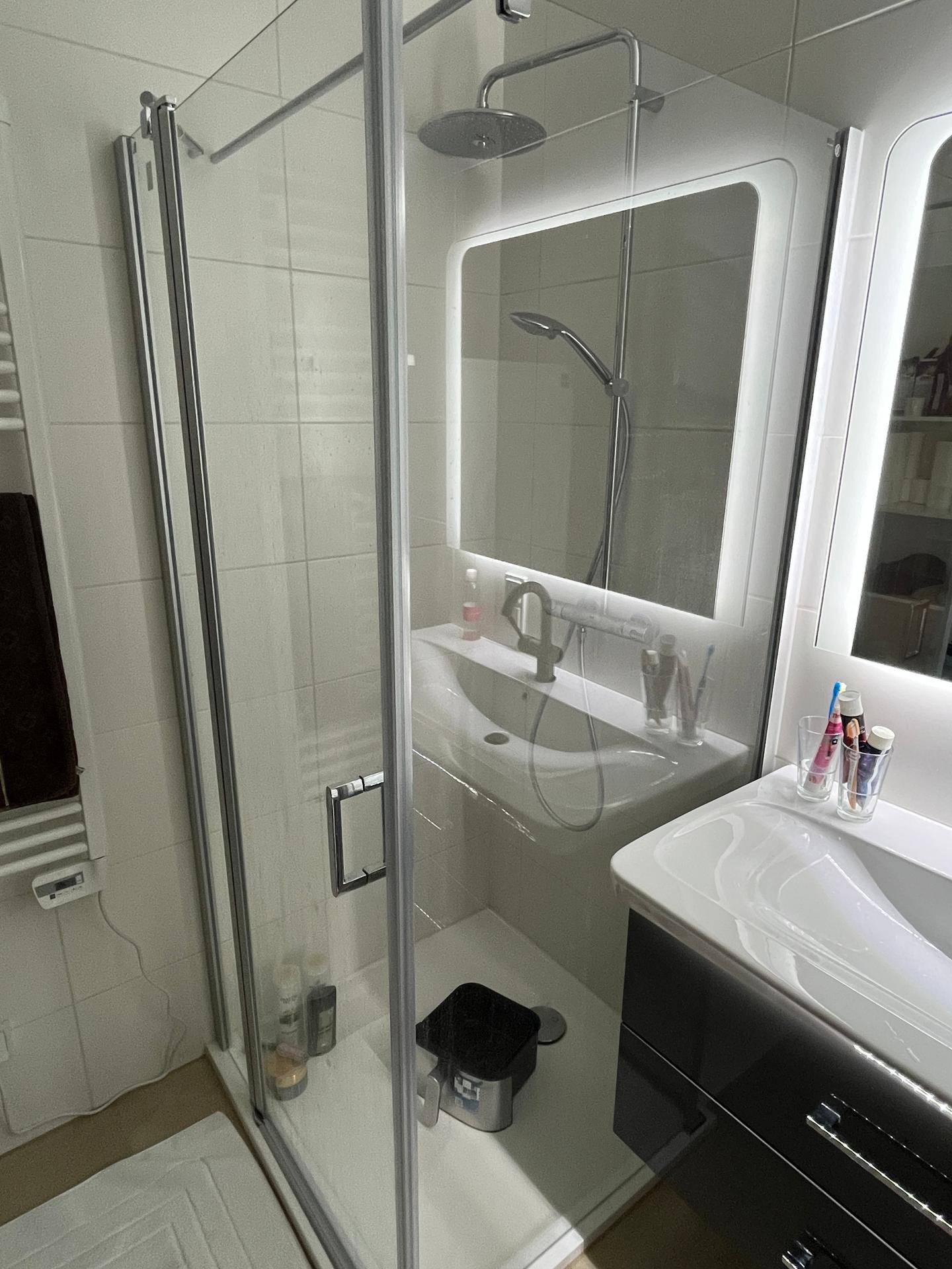 Modernes Badezimmer mit Duschkabine, beleuchtetem Spiegel und elegantem Waschbecken.