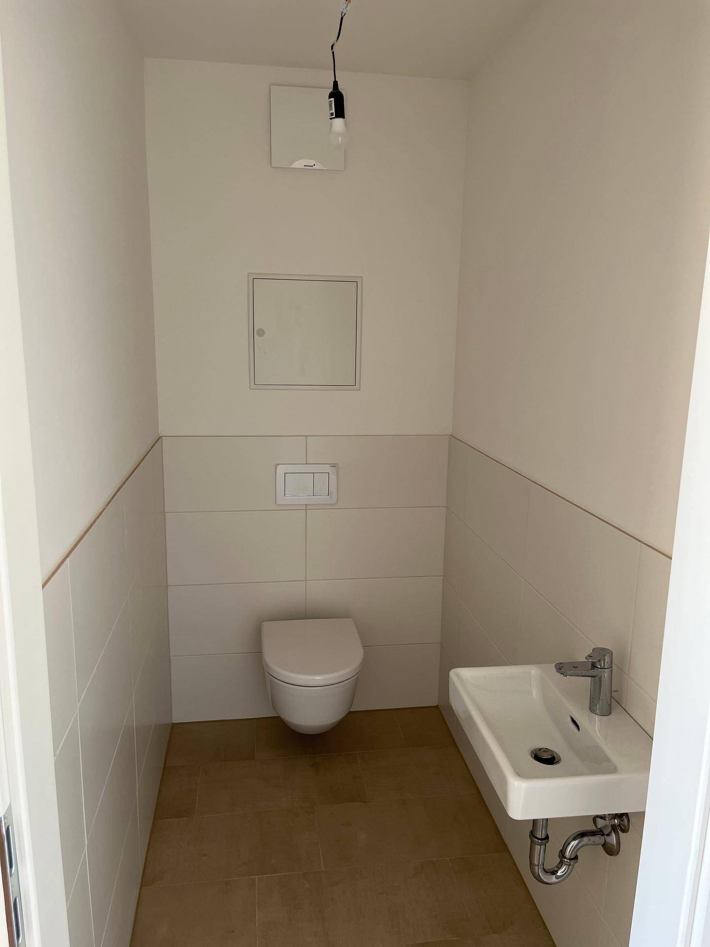 Modernes Gäste-WC mit wandhängendem WC und kleinem Waschbecken, hell gefliest.