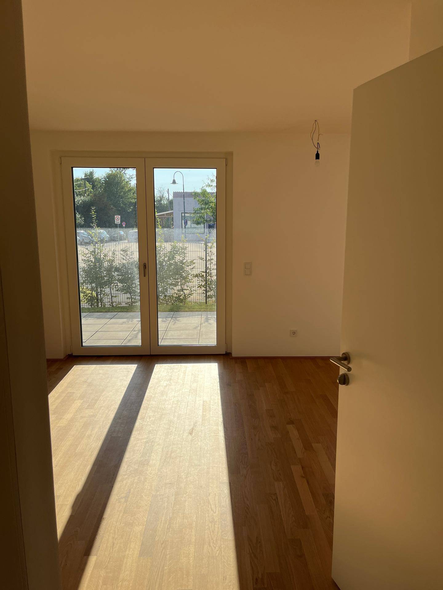 Großes, helles Zimmer mit Parkettboden und breiter Glastür zum Außenbereich.