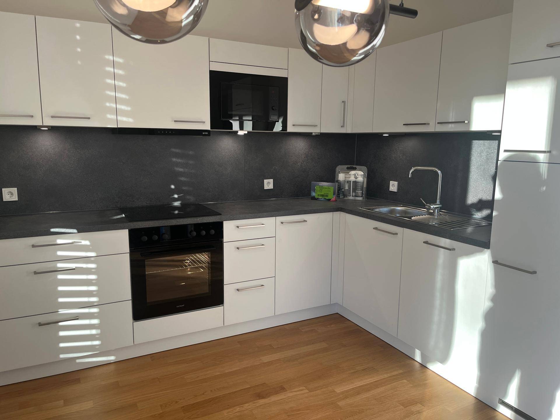 Moderne Küche mit weißen Schränken, dunkler Arbeitsplatte und Holzboden, ausgestattet mit Einbaugeräten.