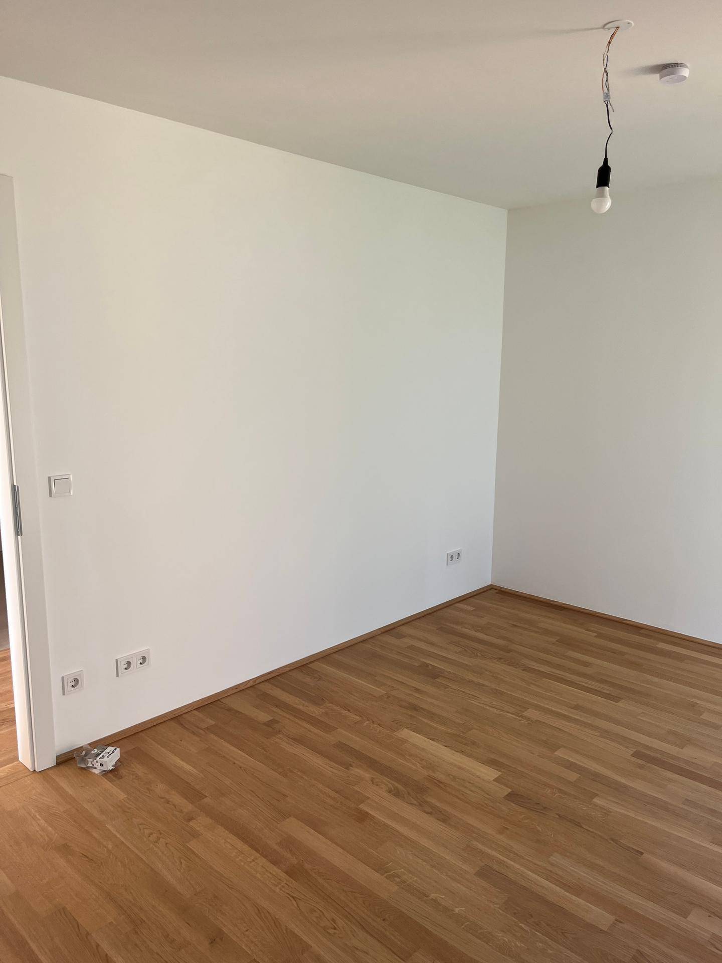 Geräumiges Zimmer mit hellem Parkettboden und weißen Wänden, ideal als Schlafzimmer.