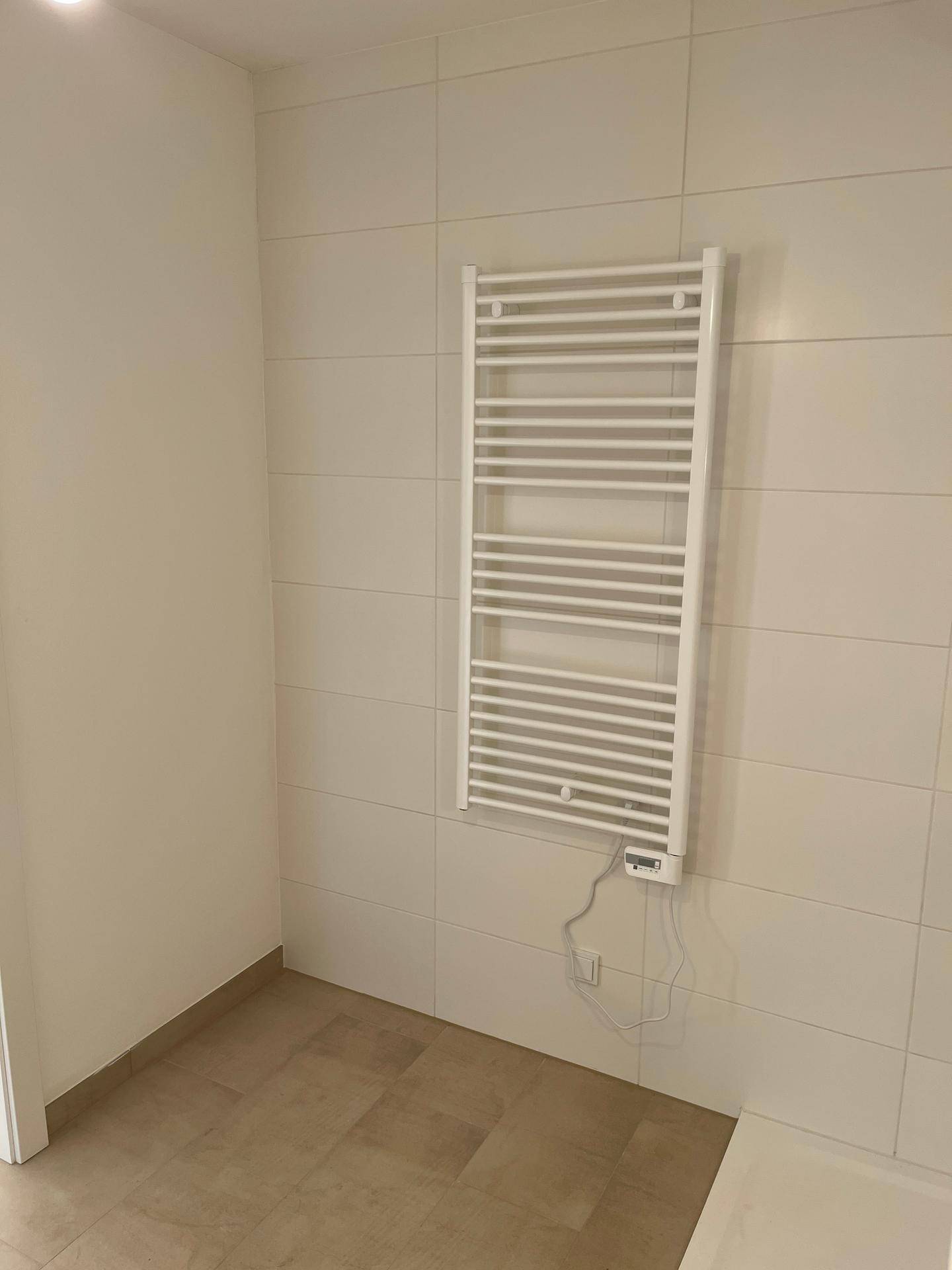 Modernes Badezimmer mit weißen Fliesen und praktischem beheiztem Handtuchhalter.