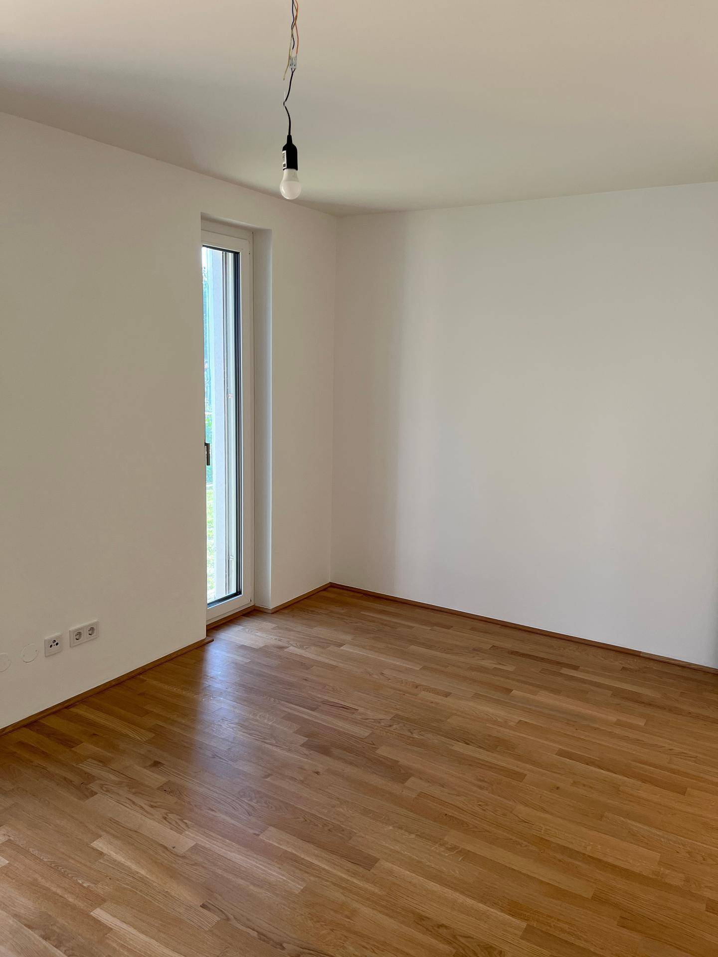 Helles Zimmer mit Parkettboden und großem Fenster, ideal als ruhiges Schlafzimmer.