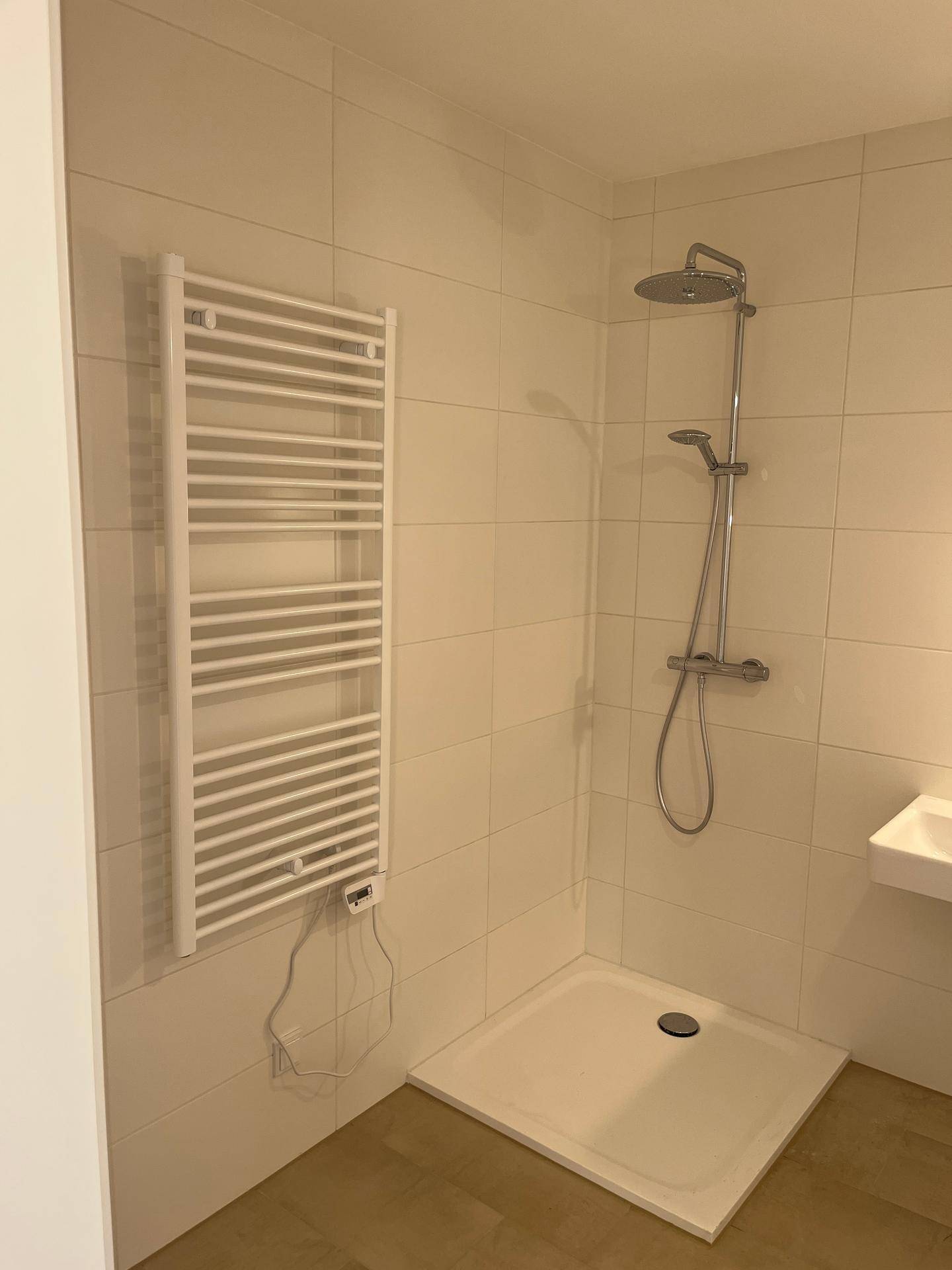 Modernes Badezimmer mit ebenerdiger Dusche und beheiztem Handtuchhalter, hell gefliest.