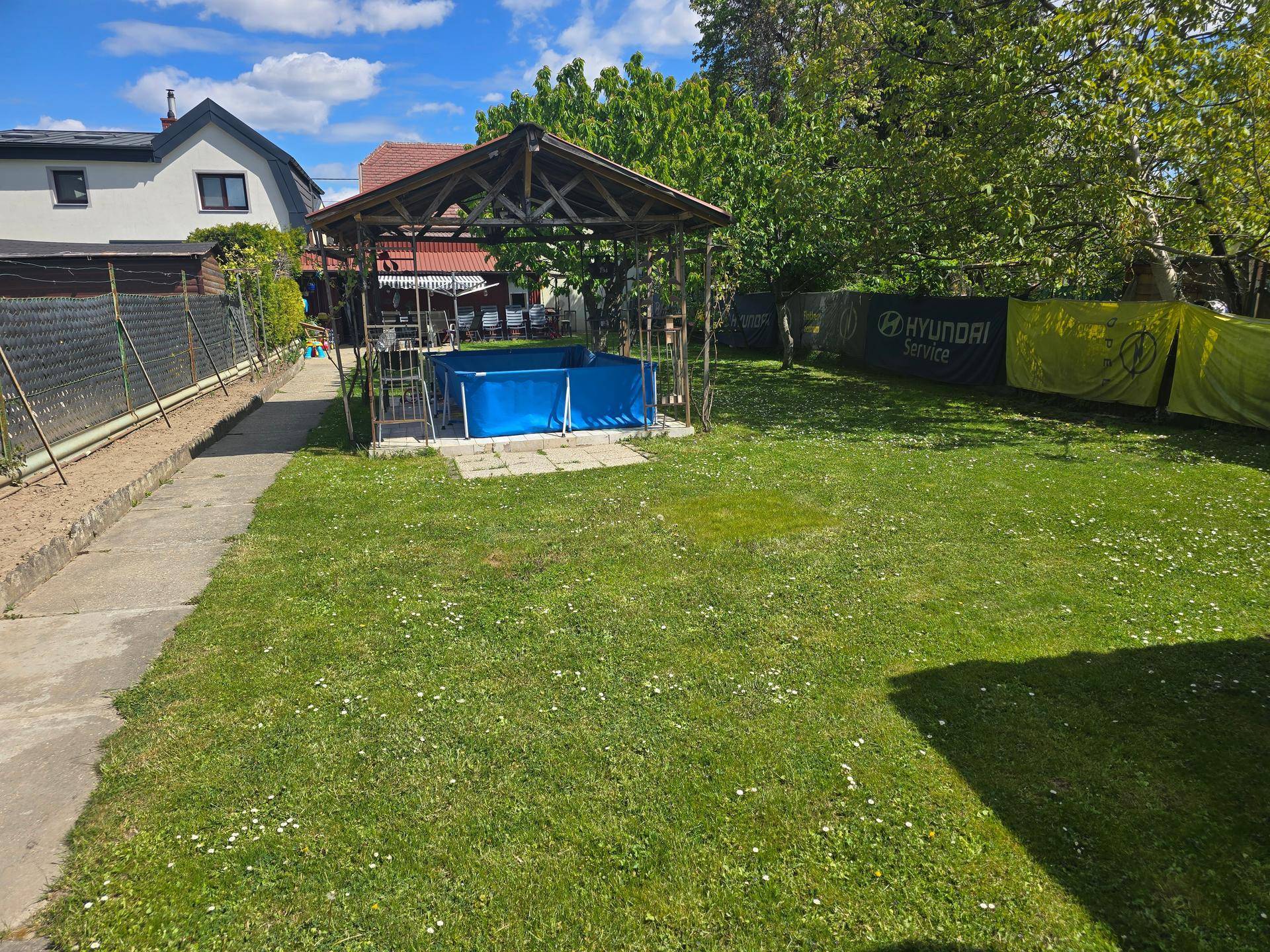 Großer Garten mit Rasenfläche, Pavillon und einem Aufstellpool unter blauem Himmel.
